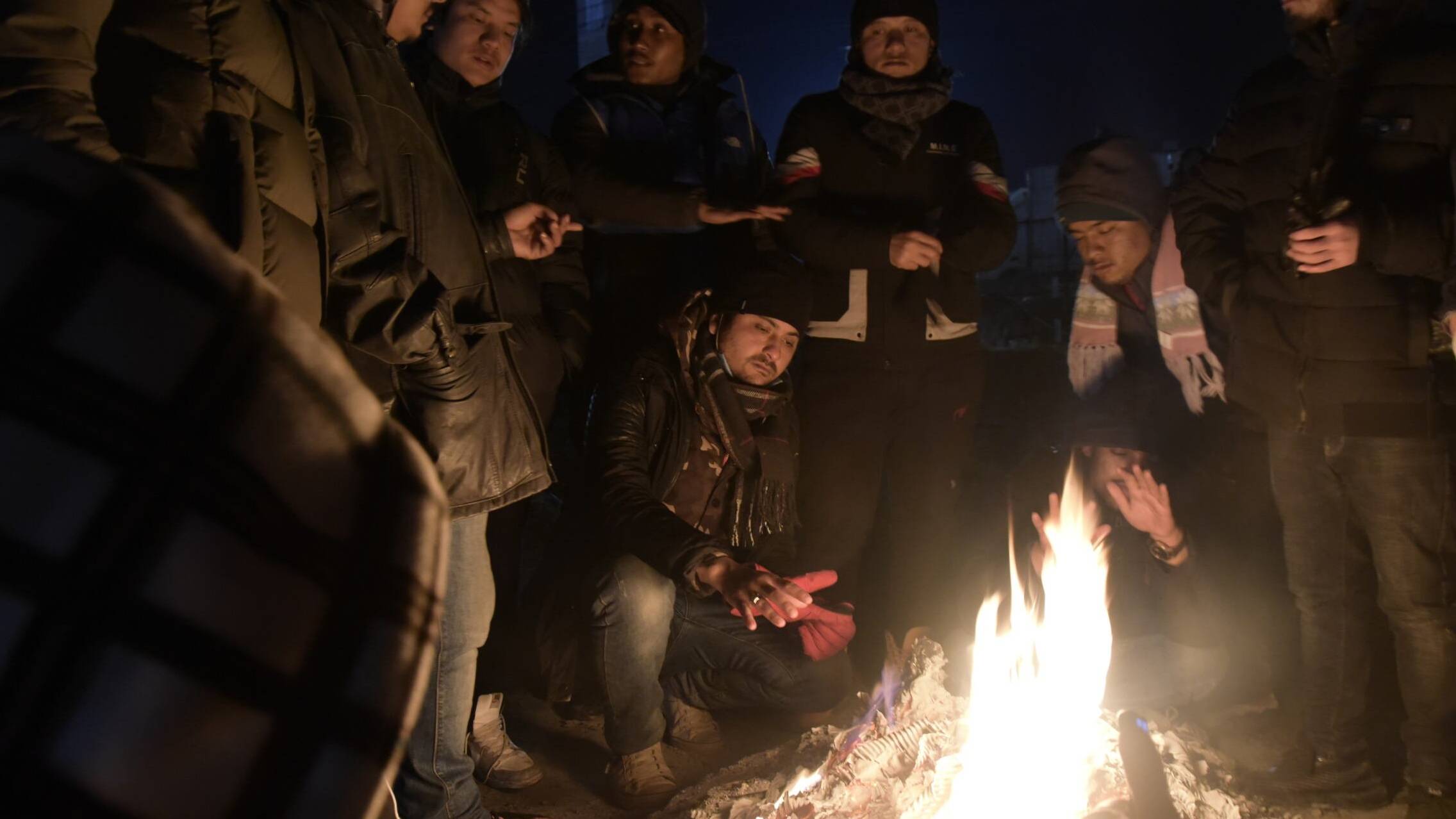 grupa uchodźców siedzi wokół ogniska w Medyce