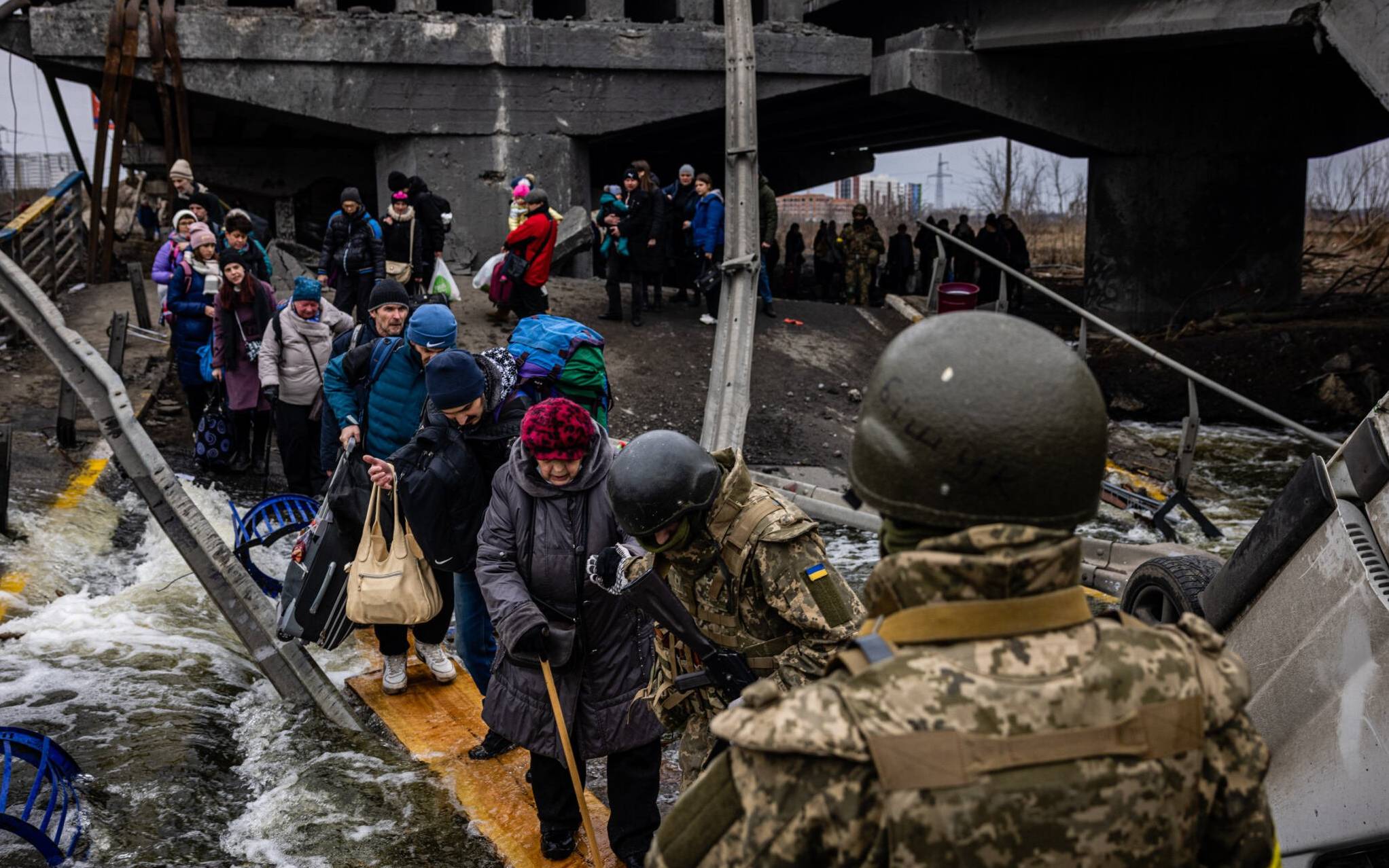 Evacuees cross a destroyed bridge as they flee the city of Irpin, northwest of Kyiv, on March 7, 2022. - Ukraine dismissed Moscow's offer to set up humanitarian corridors from several bombarded cities on Monday after it emerged some routes would lead refugees into Russia or Belarus. The Russian proposal of safe passage from Kharkiv, Kyiv, Mariupol and Sumy had come after terrified Ukrainian civilians came under fire in previous ceasefire attempts. (Photo by Dimitar DILKOFF / AFP)