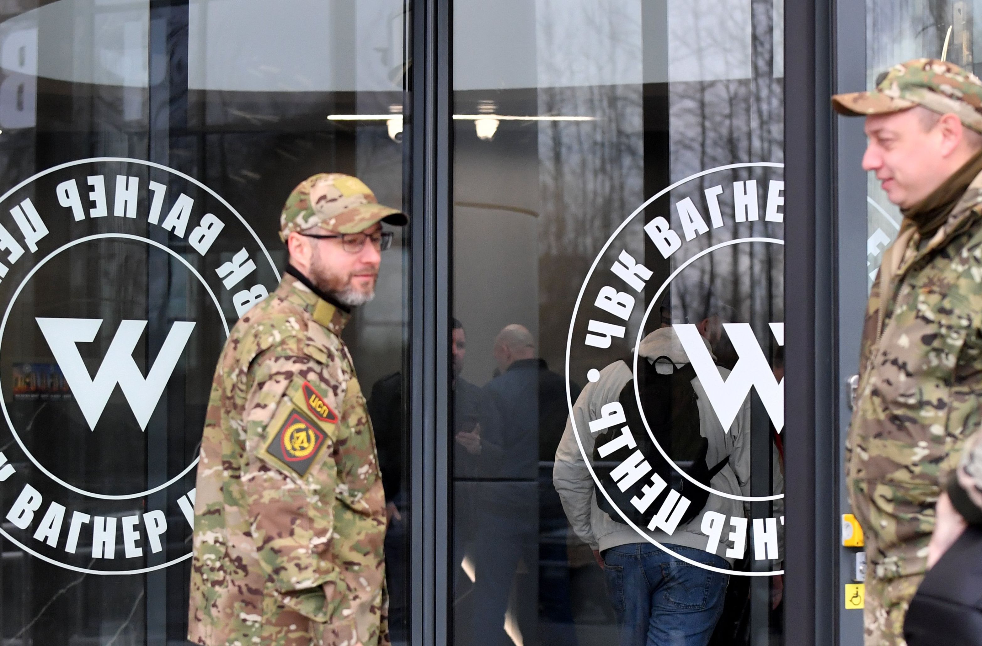 Mężczyzna w uniformie wojskowym przechodzi przez drzwi z napisem Wagner
