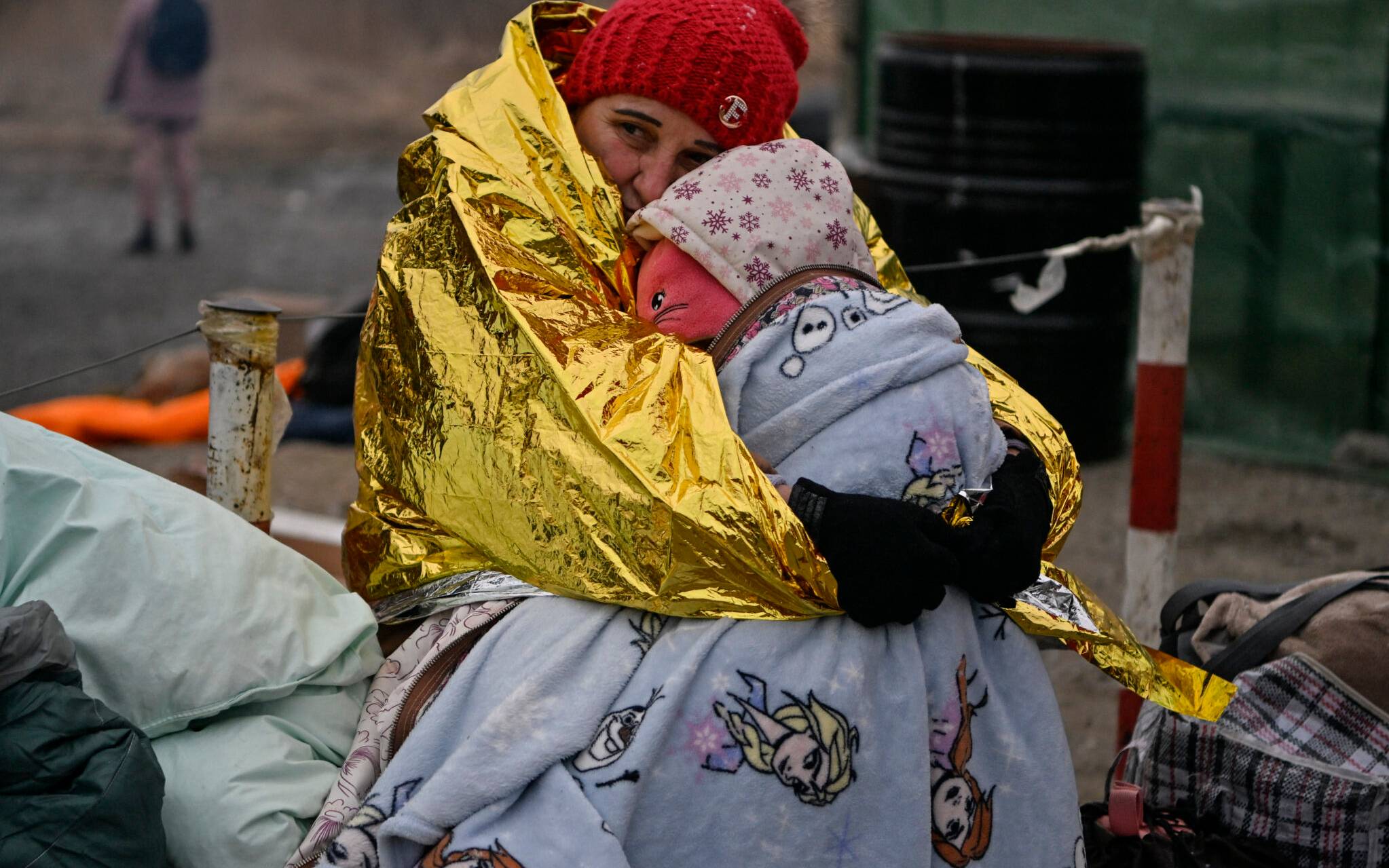 A woman hugs her grandaugther as people wait in freezing cold temperatures to be transferred to a train station, after crossing the Ukrainian borders into Poland, at the Medyka border crossing in Poland, on March 7, 2022. - More than 1,5 million people have fled Ukraine since the start of the Russian invasion, according to the latest UN data on March 6, 2022. (Photo by Louisa GOULIAMAKI / AFP)