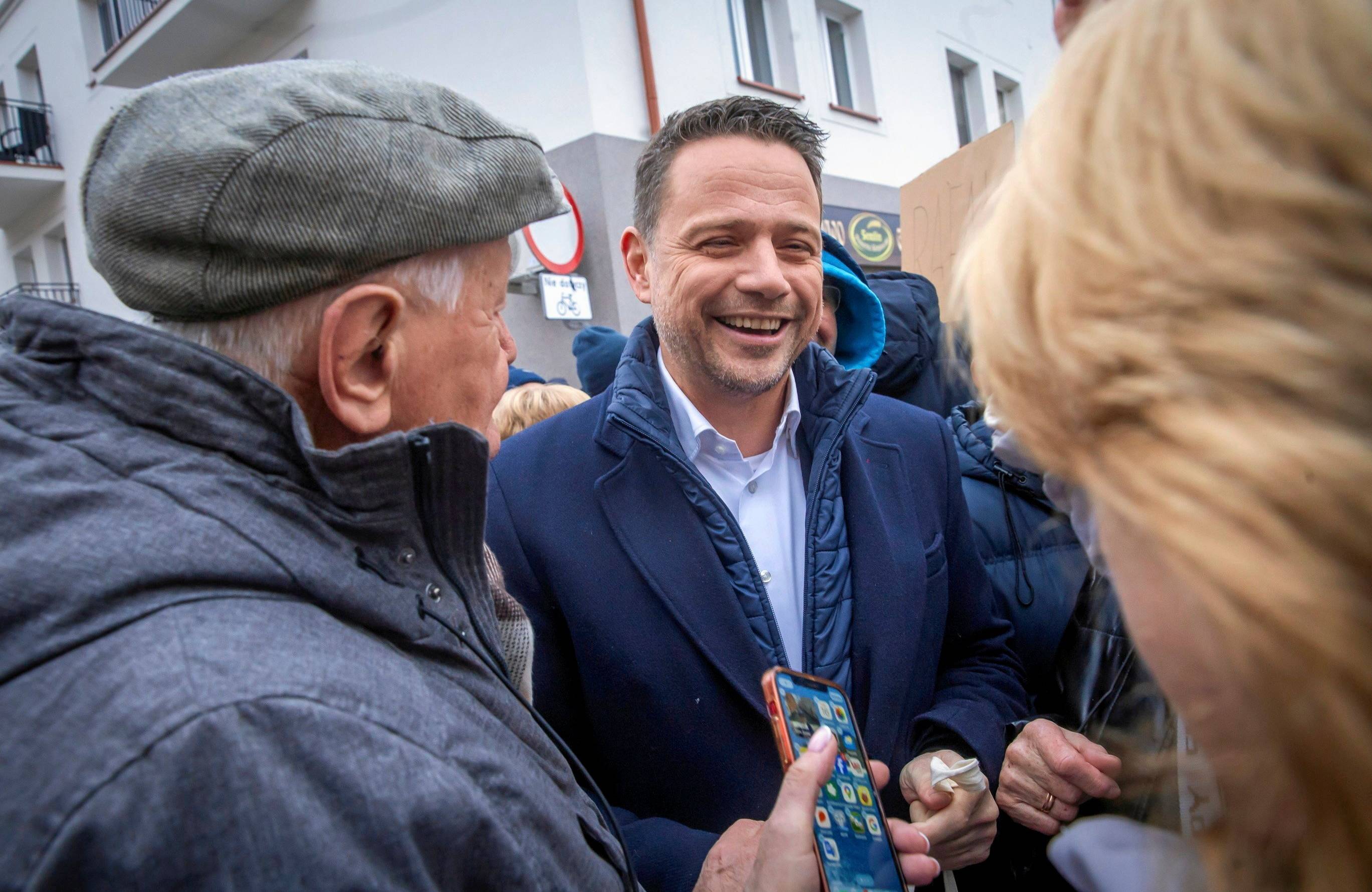 Uśmiechnięty mężczyzna rozmawia z dwójką ludzi stojących tyłem do obiektywu