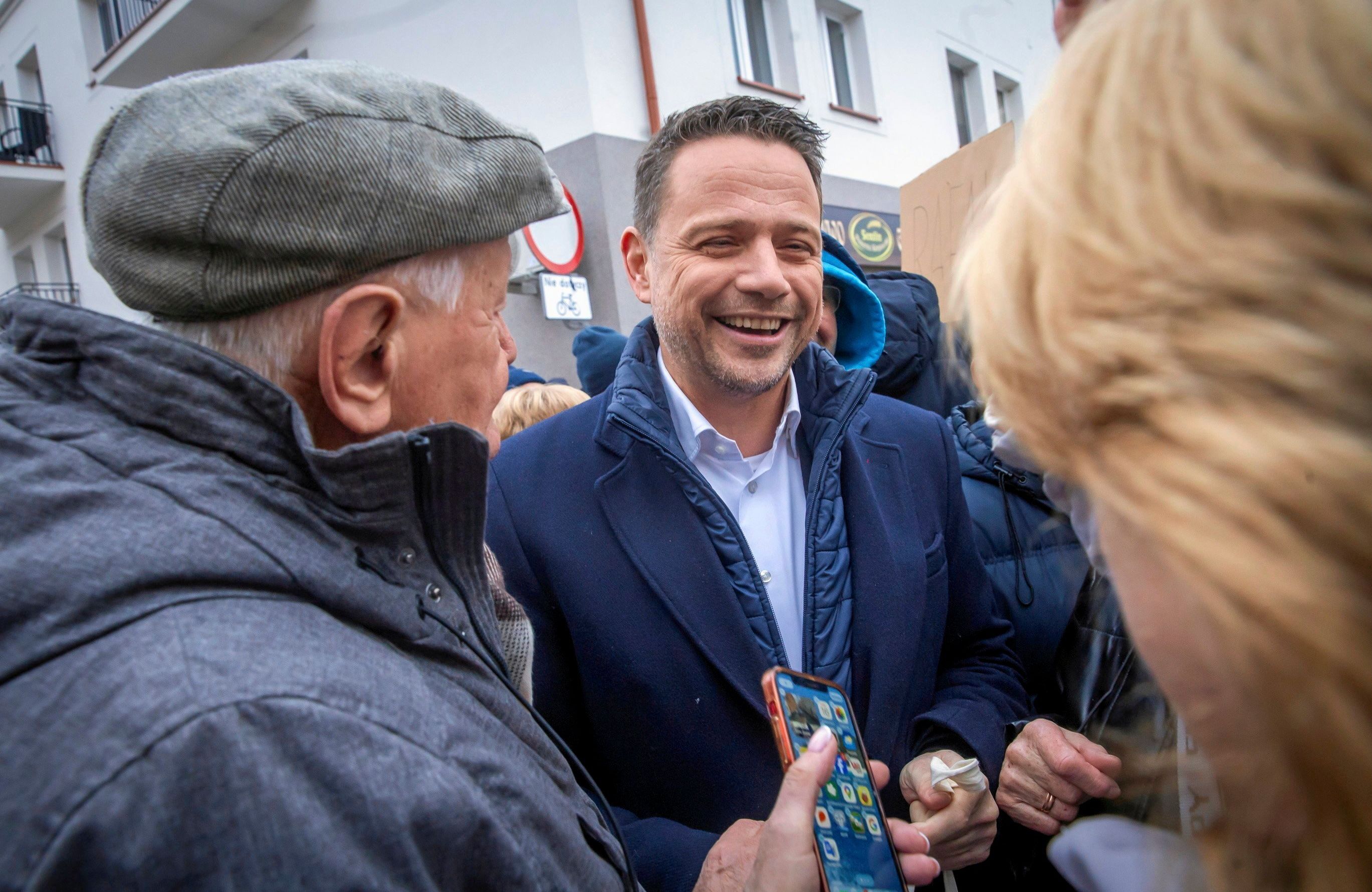 Uśmiechnięty mężczyzna rozmawia z dwójką ludzi stojących tyłem do obiektywu