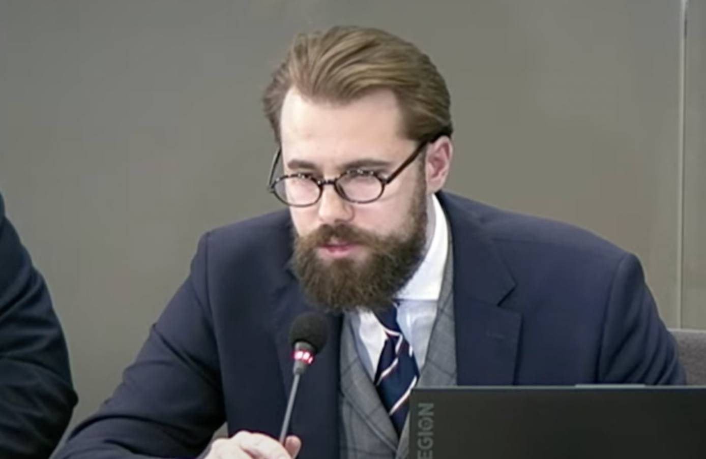 Jakub Osajda podczas przesłuchania przed komisją ds. afery wizowej. Ma brodę i ciemne, okrągłe oprawki okularów