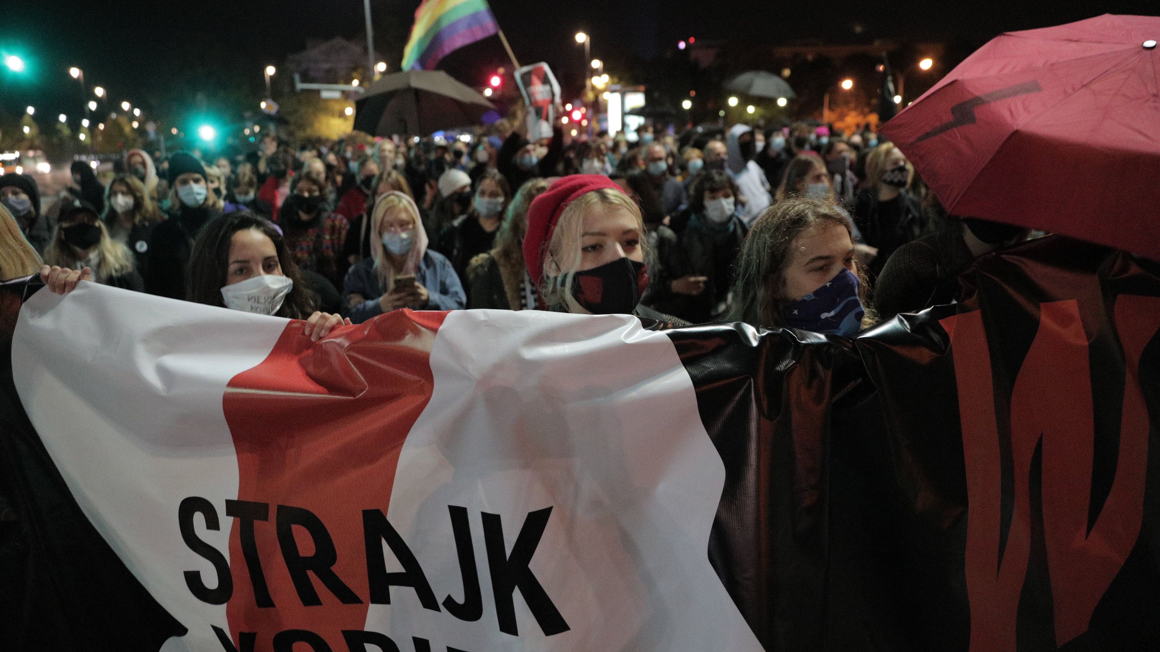 Tłum ludzi wieczorem z banerem Strajk Kobiet