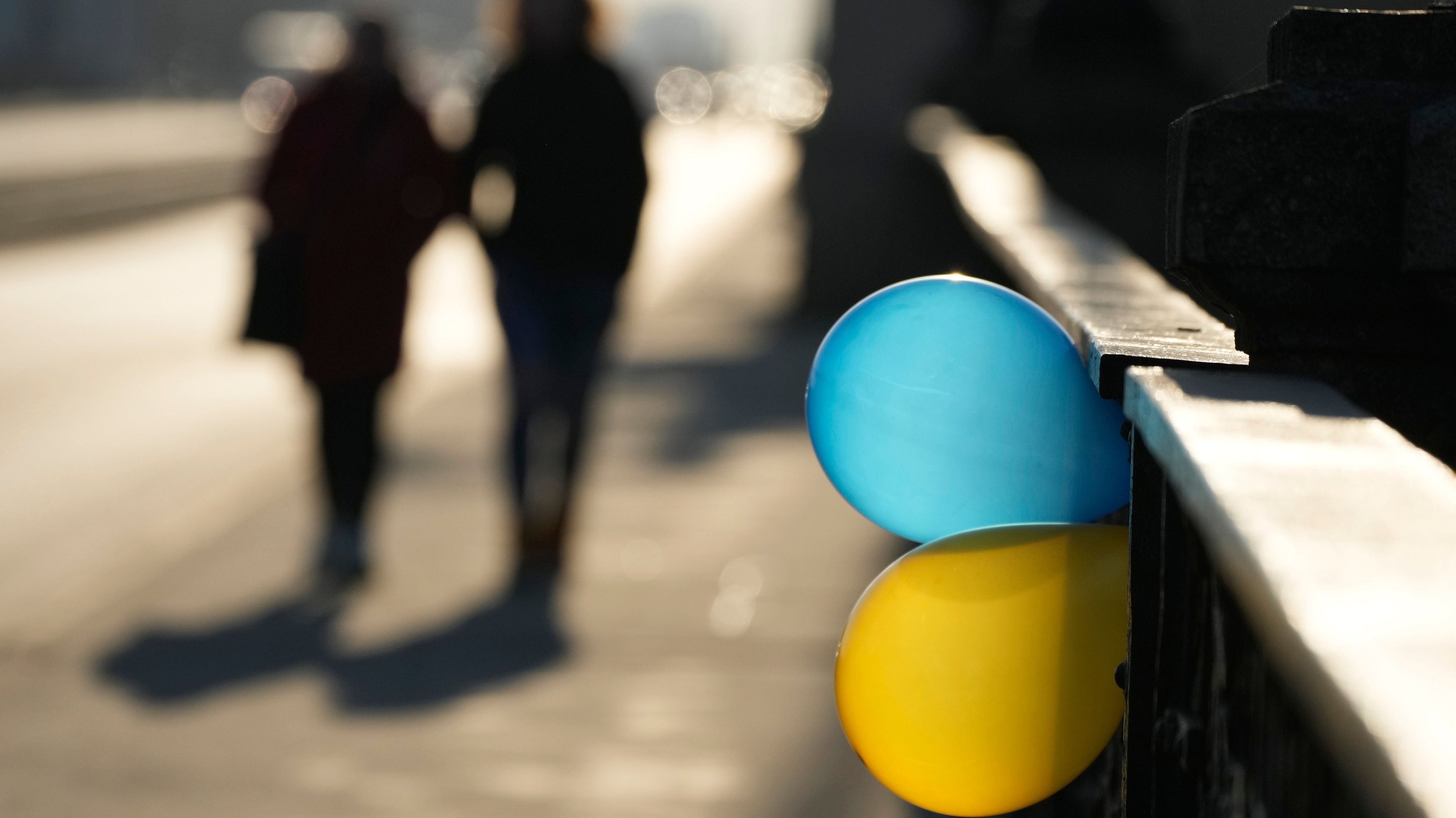 Na zdjęciu są dwa balony: niebieski i żółty, zawieszone na moście, w tle widać dwie postacie