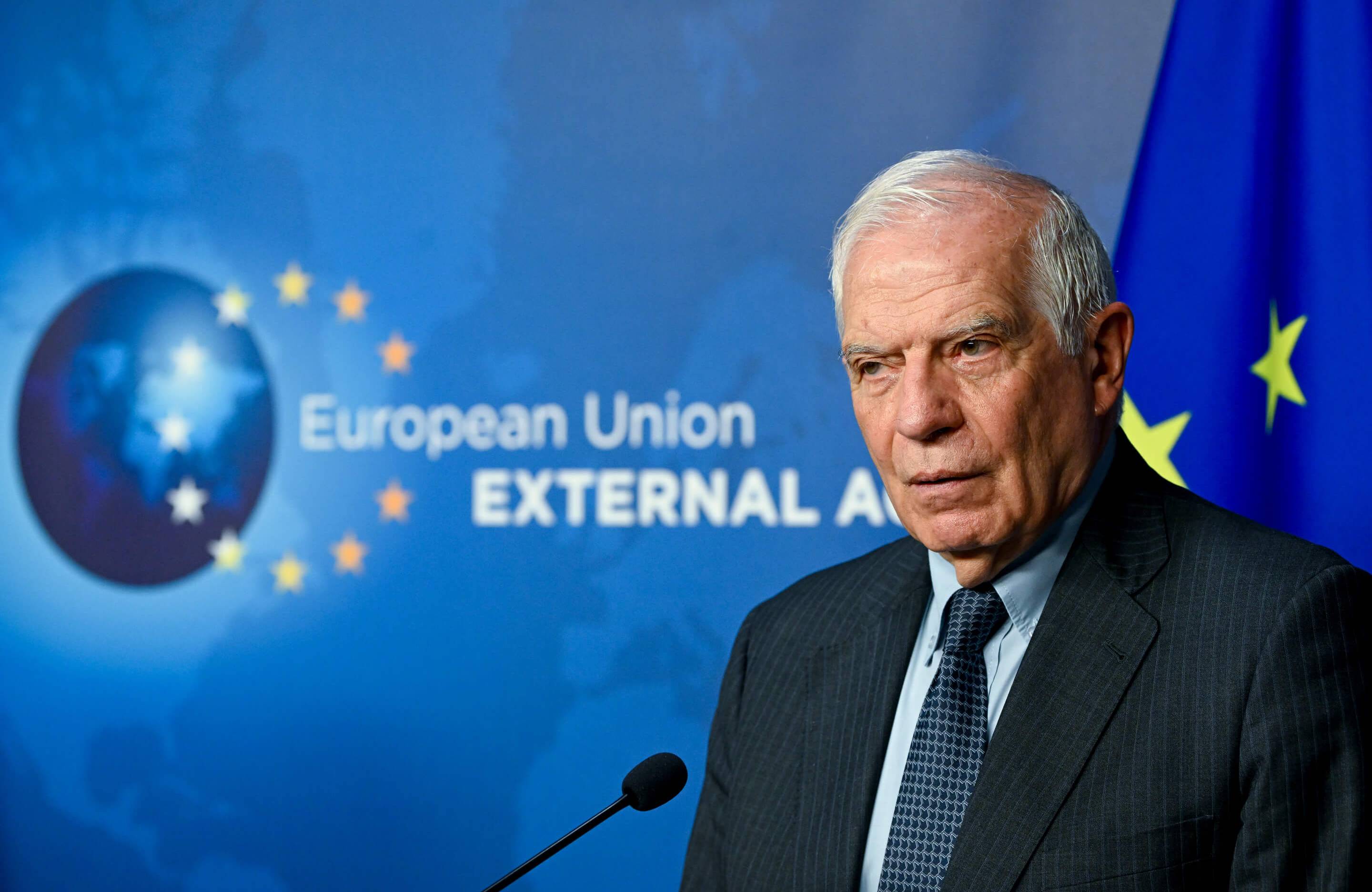 Mężczyzna o siwych włosach w czarnym garniturze na niebieskim tle z logiem Europejskiej Służby Działań Zewnętrznych