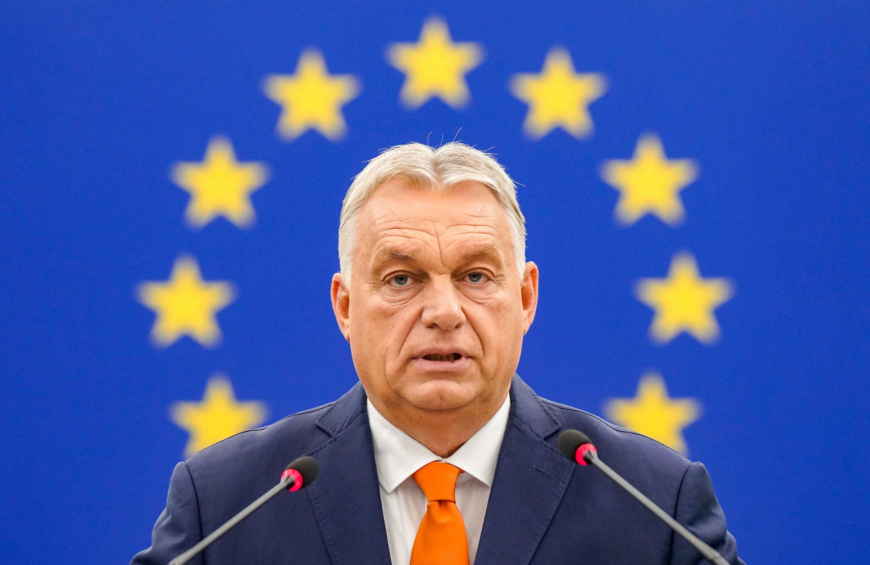 Viktor Orban sfotografowany na tle niebieskiej flagi UE; zdjęcie jest skadrowane tak, że okrąg z gwiazdek unijnej flagi układa się przy głowie premiera Węgier jak aureola.