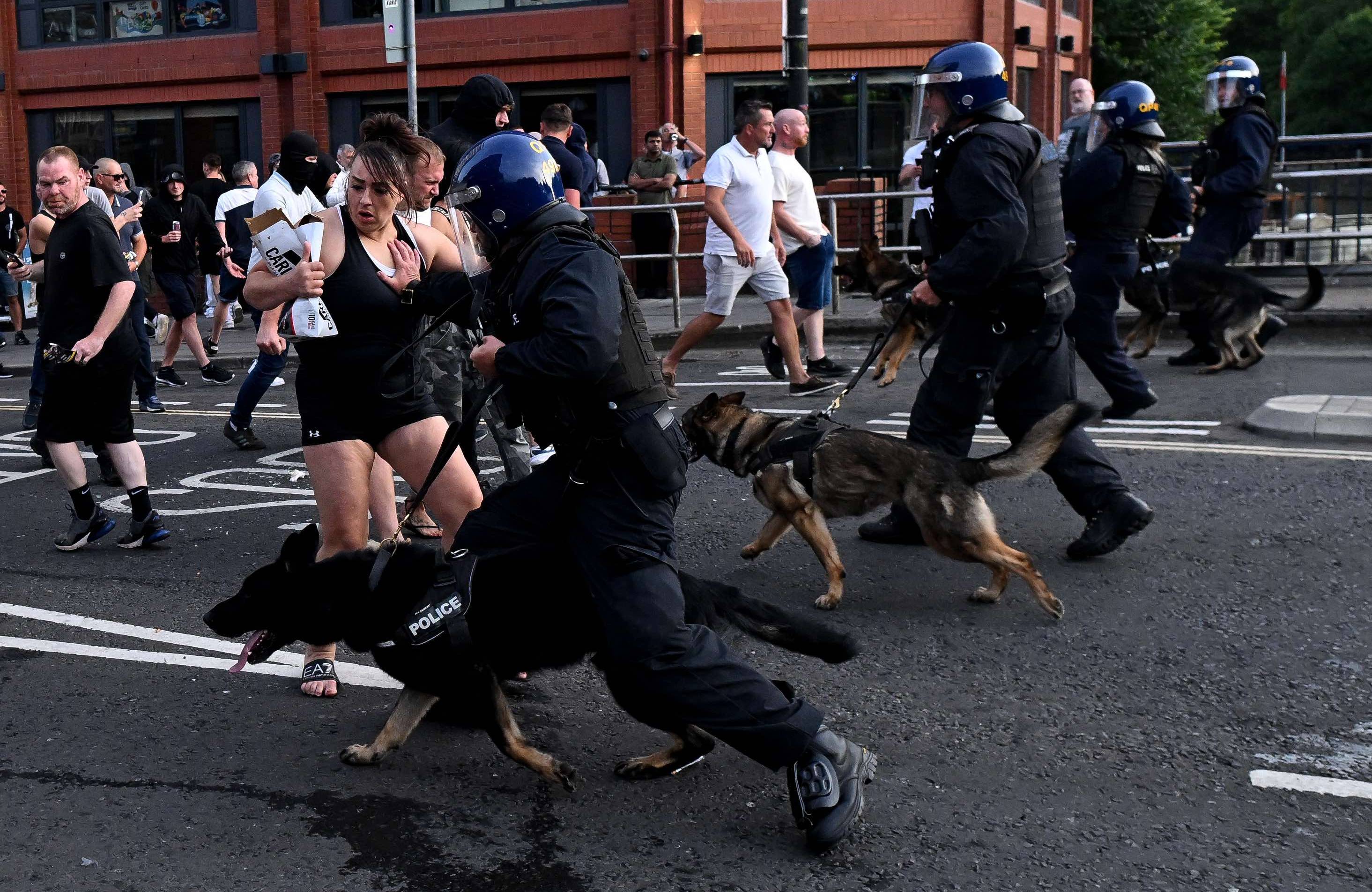 Policjanci z psami biegną w stronę demonstrantów na ulicy. Wielka Brytania