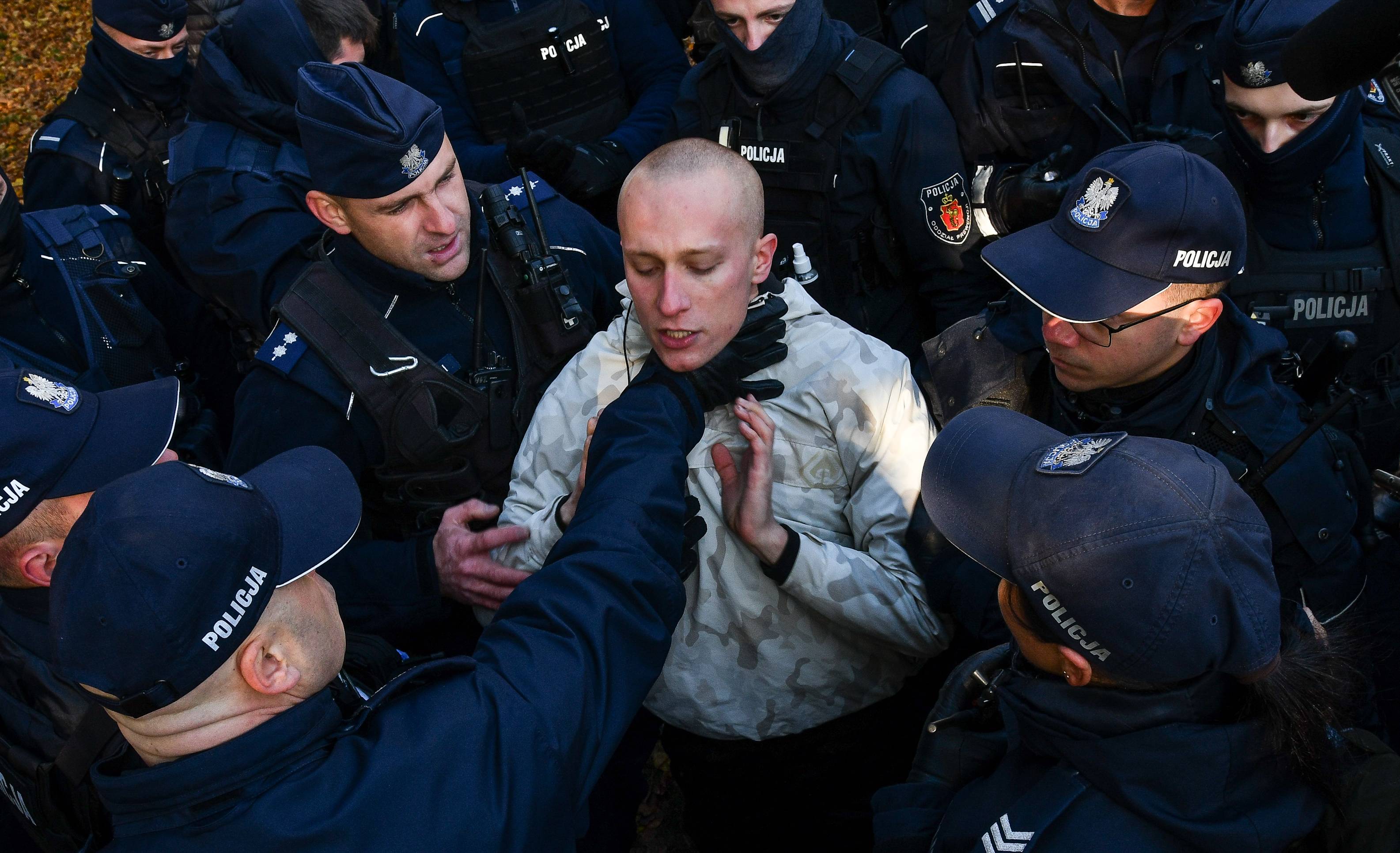 Policjant chwyta za gardło protestującego, otoczonego przez innych policjantów. Policyjna przemoc