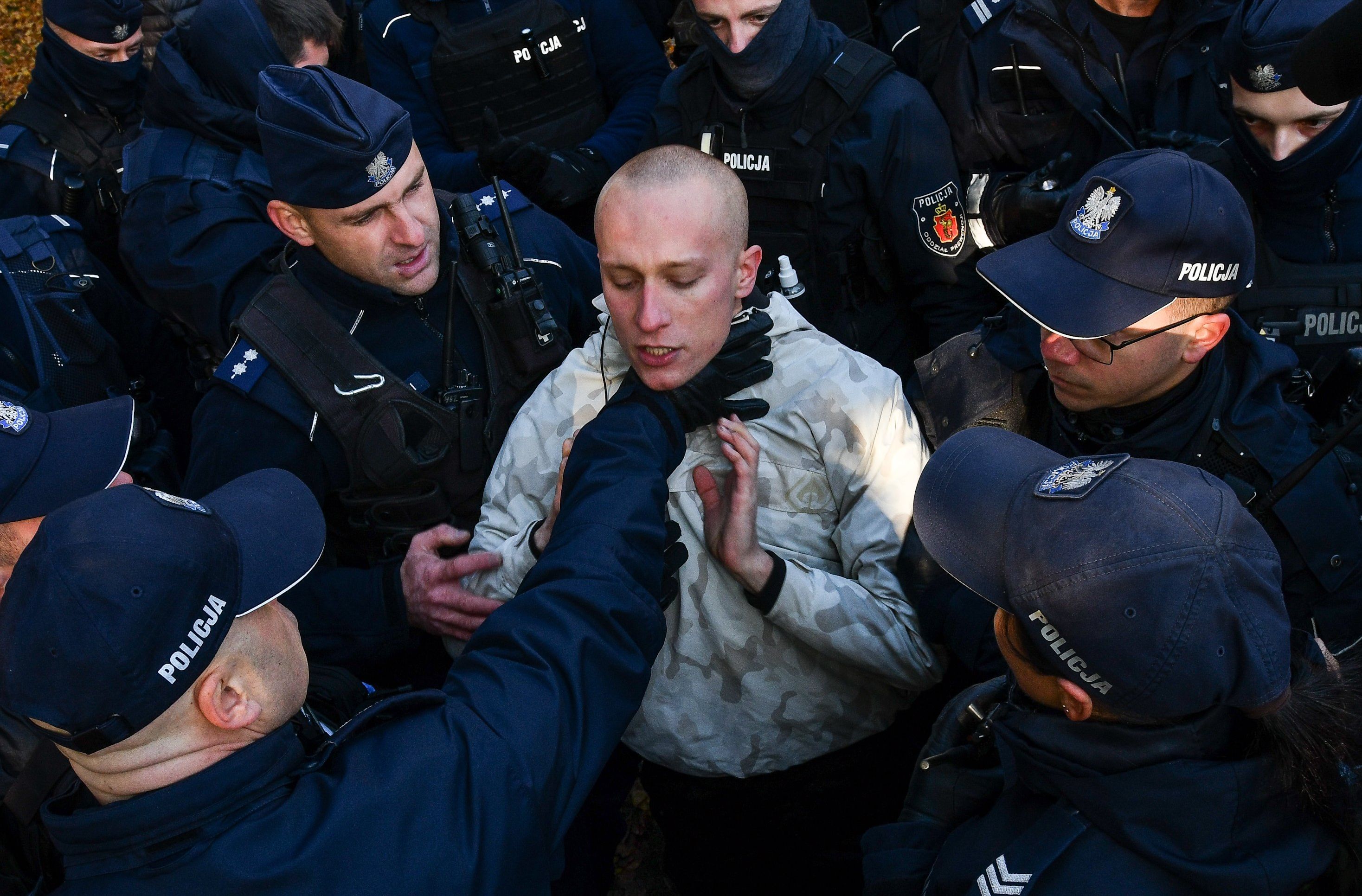 Policjant chwyta za gardło protestującego, otoczonego przez innych policjantów. Policyjna przemoc