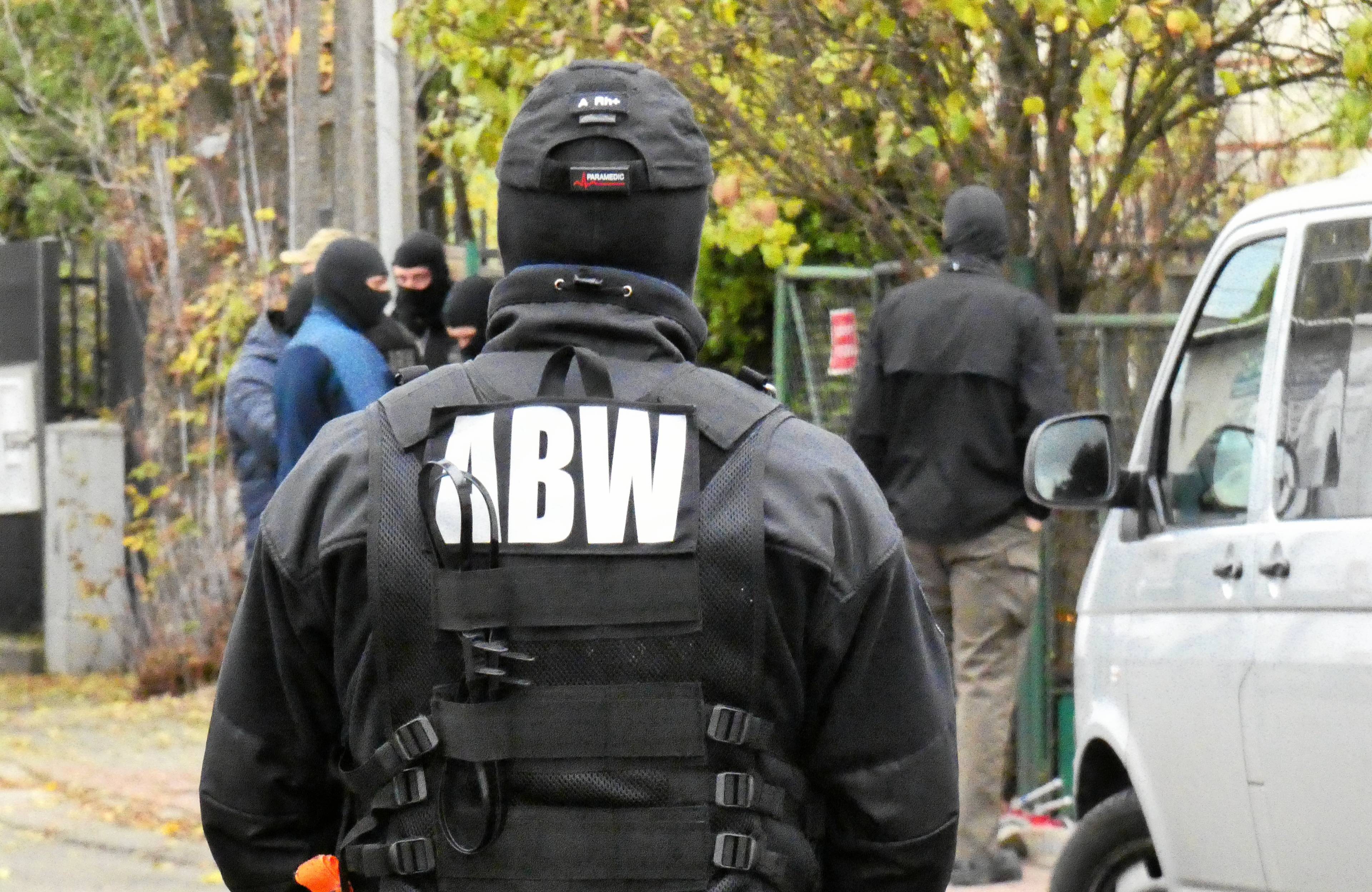 Funkcjonariusz ABW w mundurze i kamizelce z nazwą Agencji stoi tyłem do kamery.