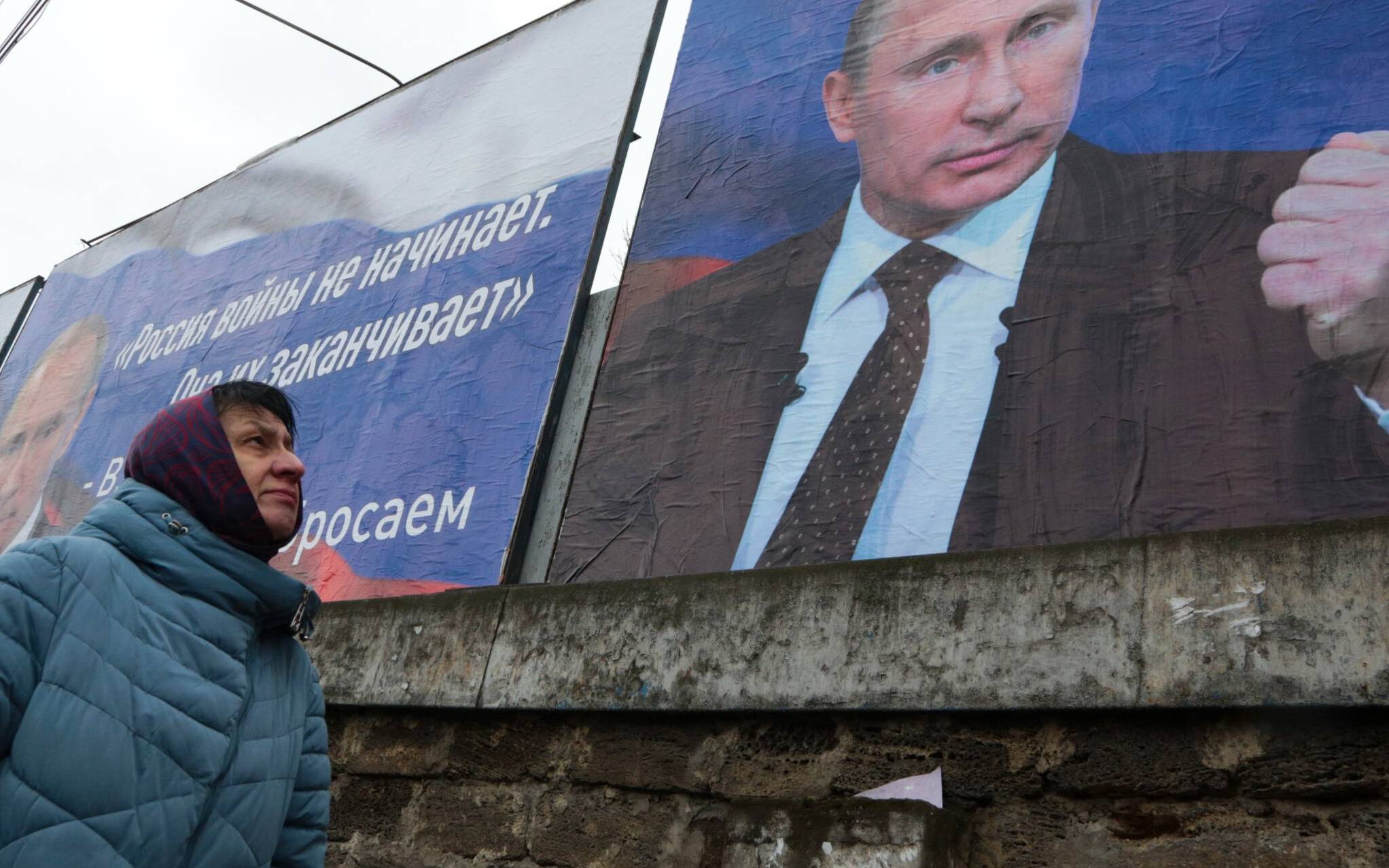 A woman walks past huge placards bearing images of Russian President Vladimir Putin and reading "Russia does not start wars, it ends them" (L) and "We will aim for the demilitarization and denazification of Ukraine" in the city center of Simferopol, Crimea, on March 4, 2022. - Ukraine accused the Kremlin of "nuclear terror" on March 4, after Europe's largest atomic power plant was attacked and taken over by invading forces, sparking Western horror at the threat of Russia's war contaminating all of Europe. (Photo by STRINGER / AFP)