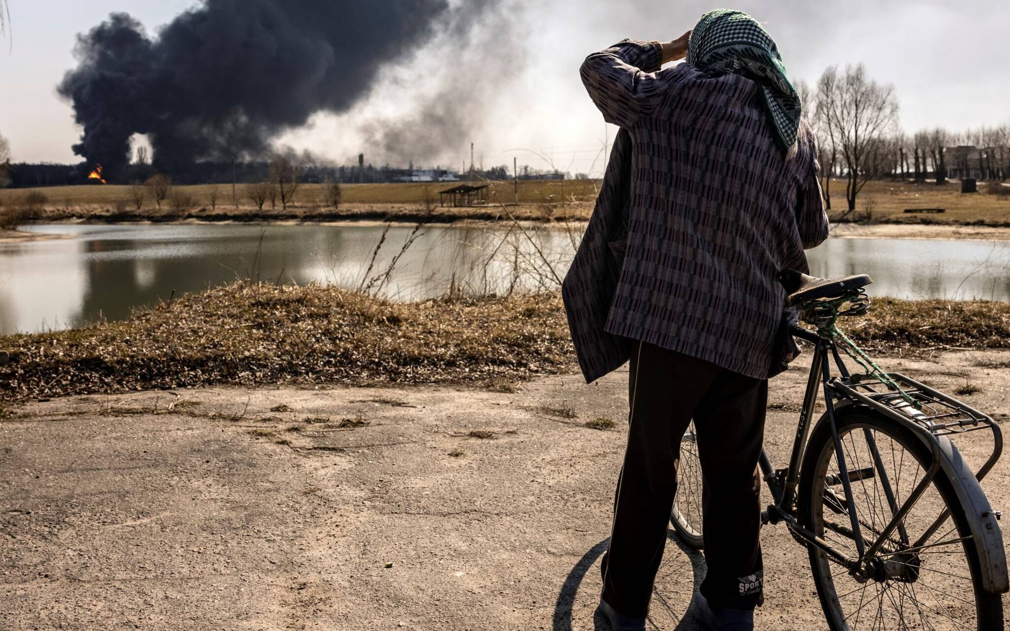 A man stands while smoke rises after Russian attacks hit a fuel storage facility in the city of Kalynivka, on March 25, 2022. (Photo by FADEL SENNA / AFP)