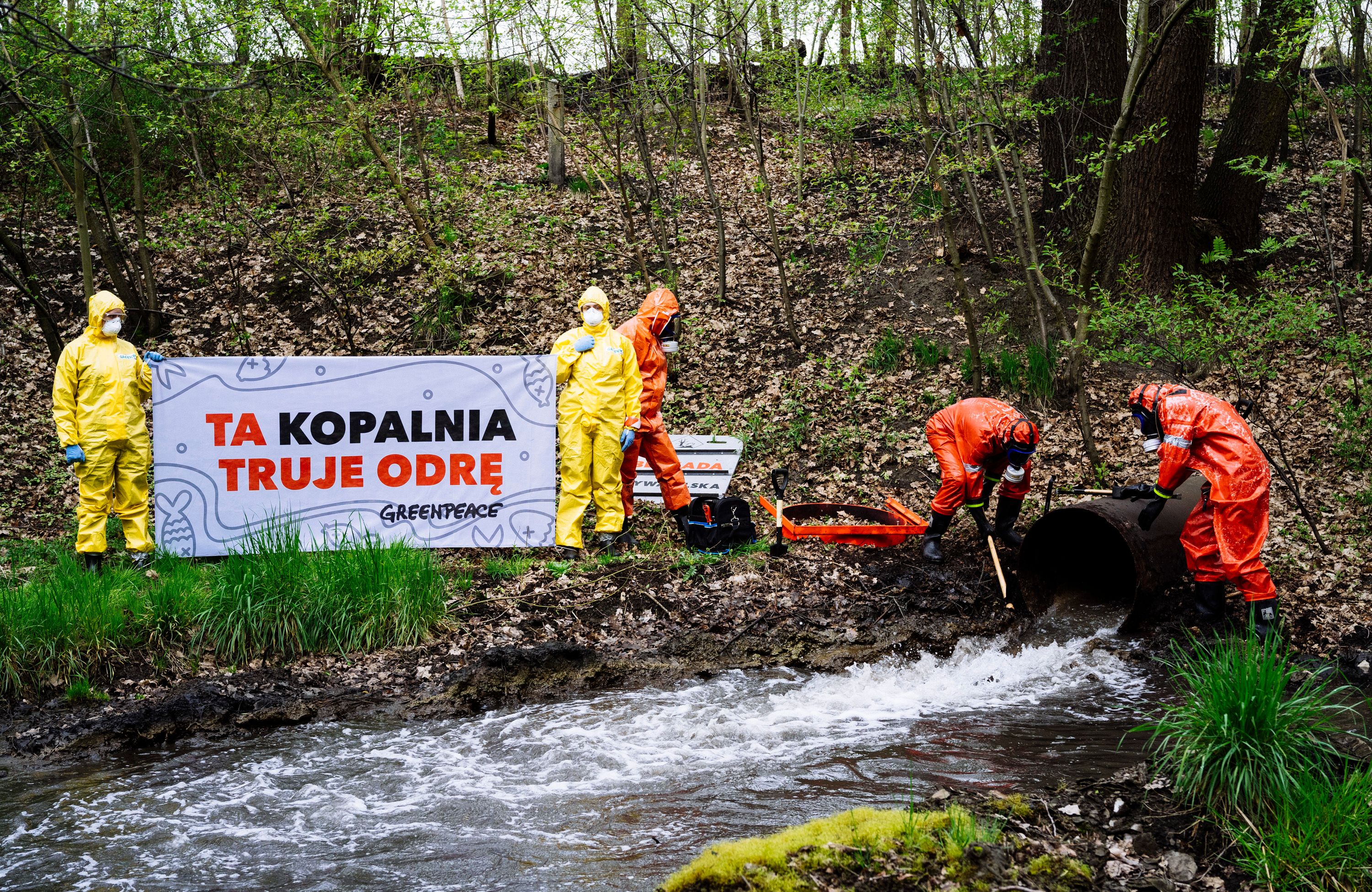 grupa aktywistów stoi nad wodą i trzyma baner z napisem "TA KOPALNIA TRUJE ODRĘ"