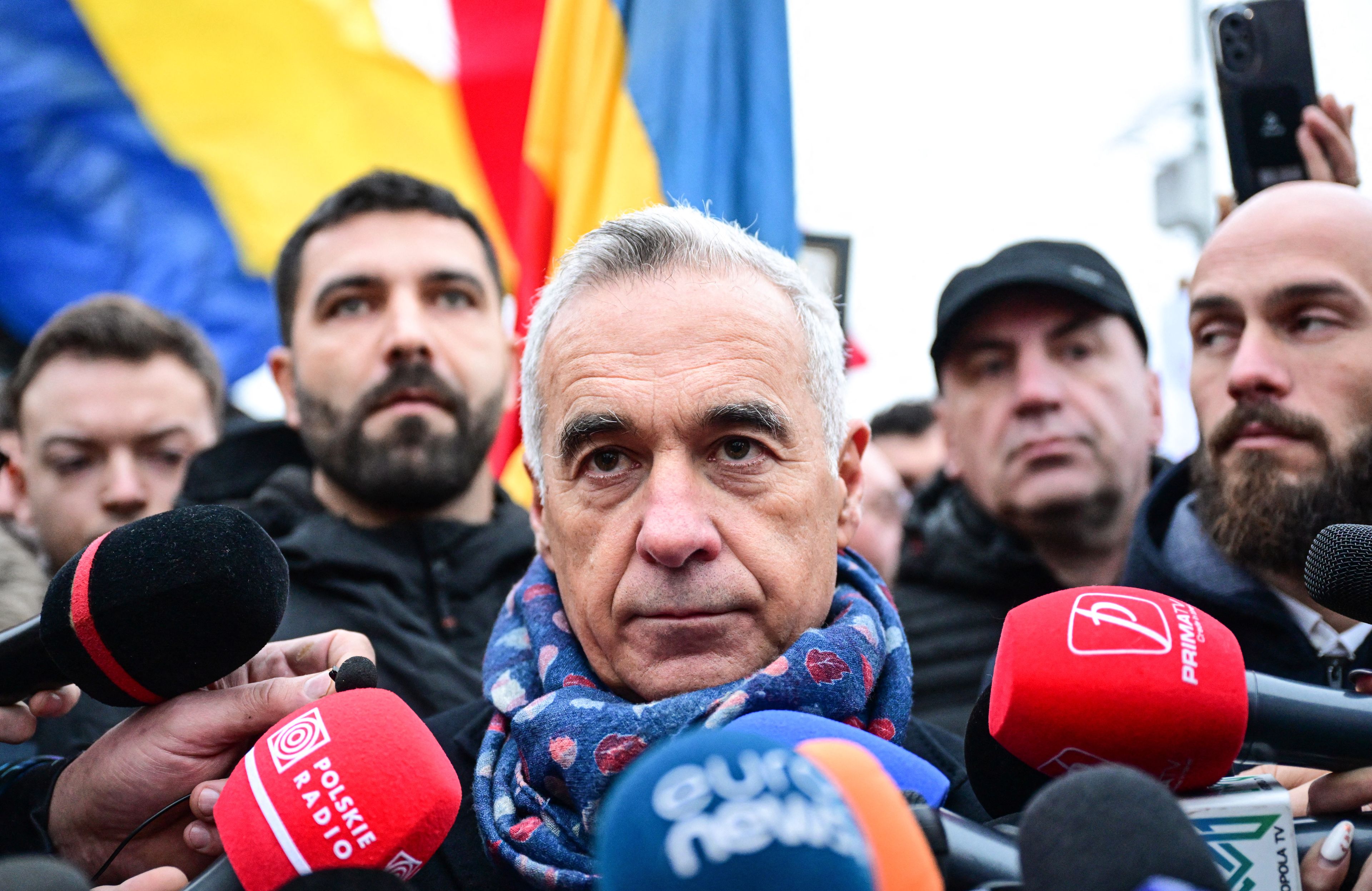 Siwy mężczyzna w szaliku w gąszczu mikrofonów