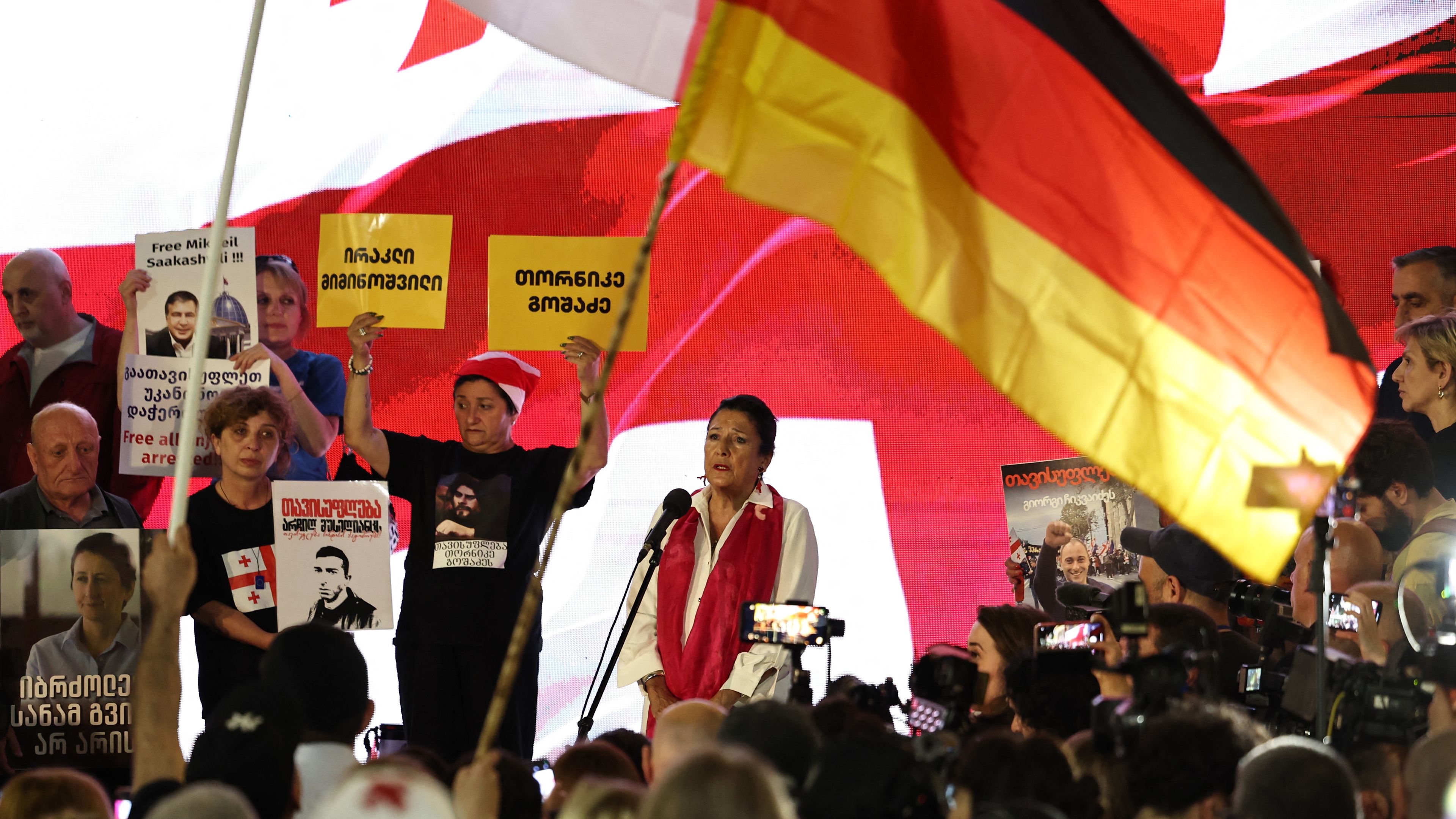 Czarnowłosa kobieta w biało-czerwonym stroju na manifestacji wśród flag.