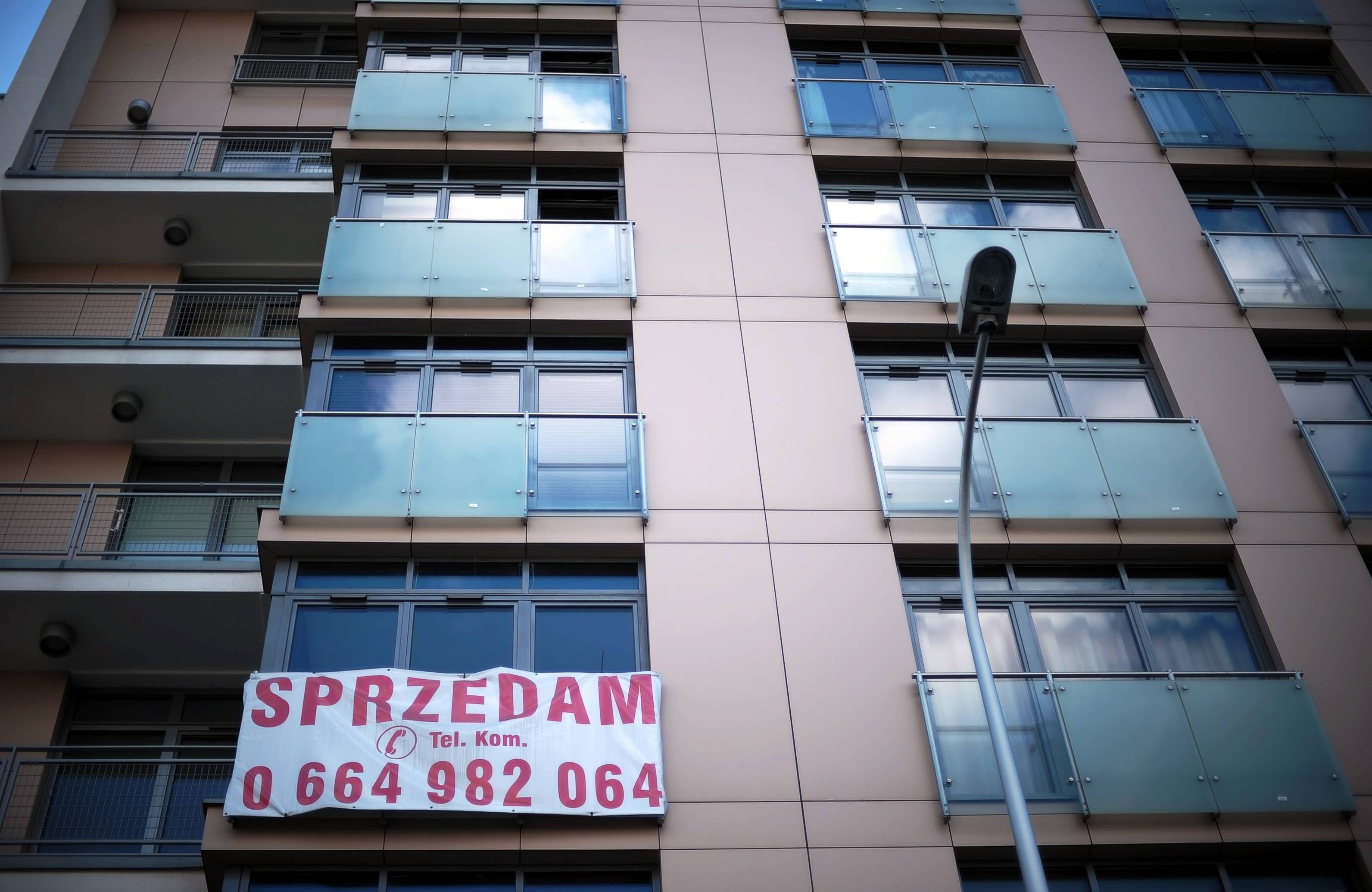 Ściana mieszkania z balkonami, na jednym płachta z napisem SPRZEDAM i numerem telefonu