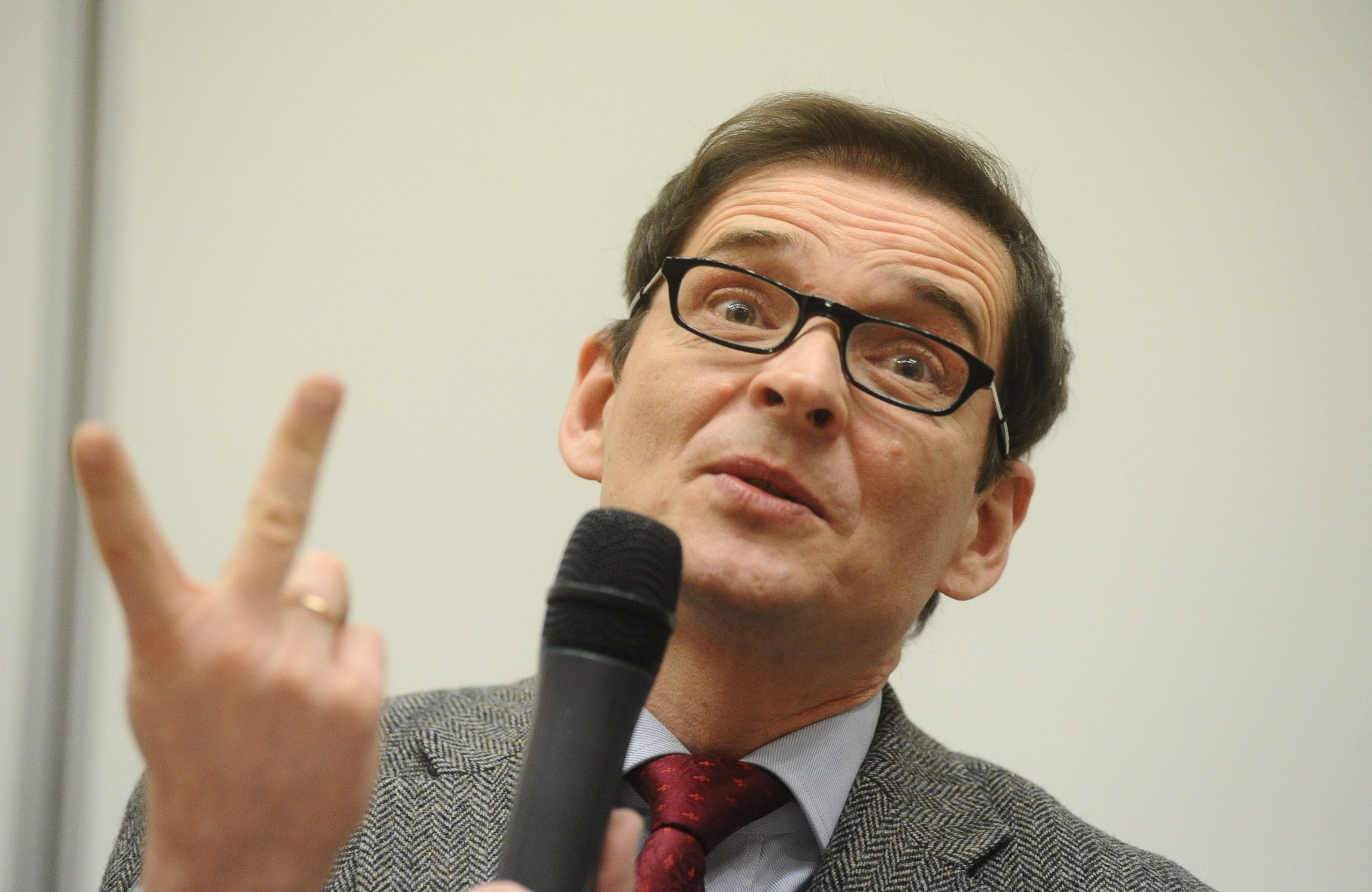 Przemysław Babiarz, mężczyzna w okulrach z mikrofonem w ręku wznosi palec do góty