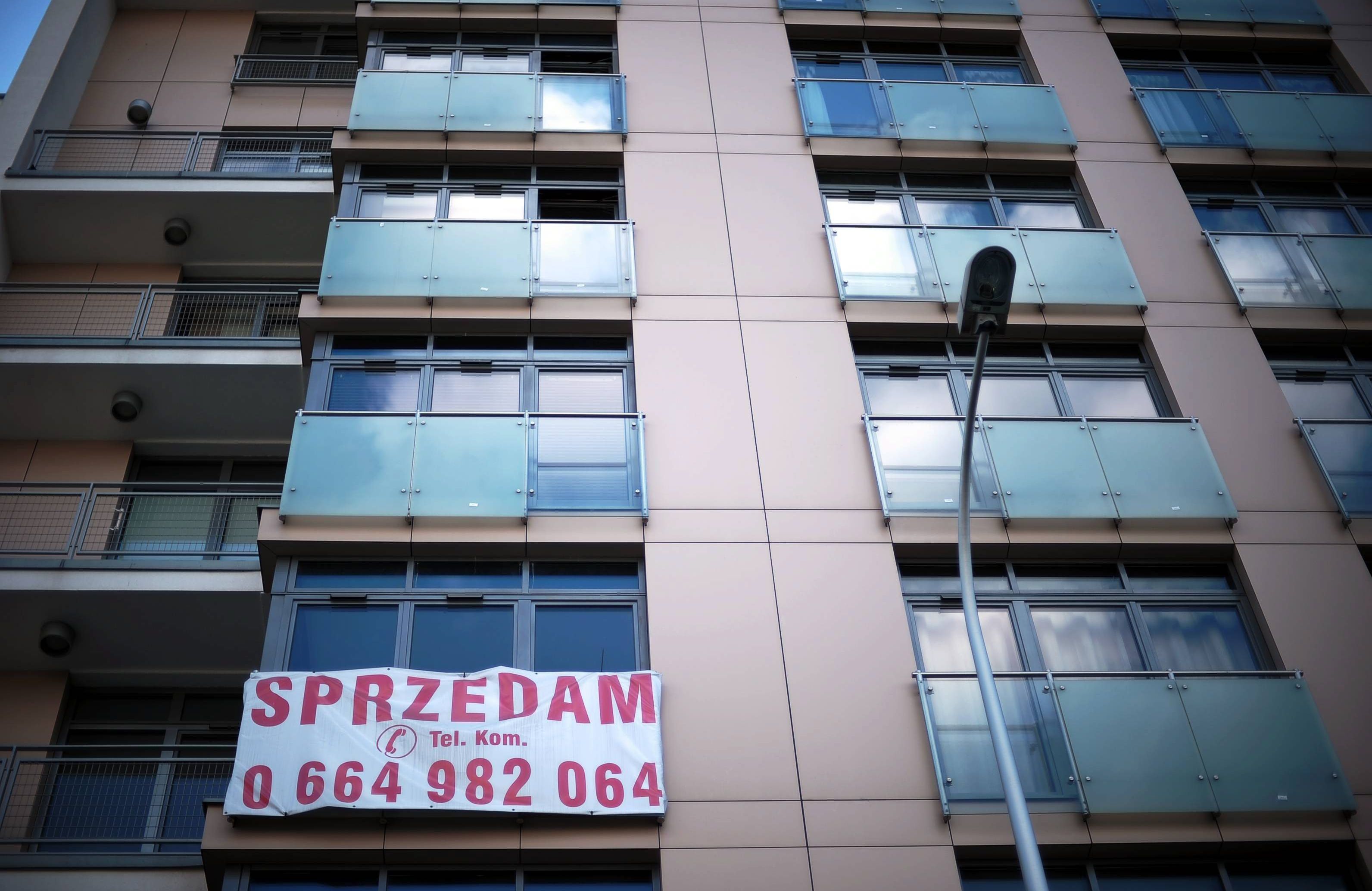 Ściana mieszkania z balkonami, na jednym płachta z napisem SPRZEDAM i numerem telefonu