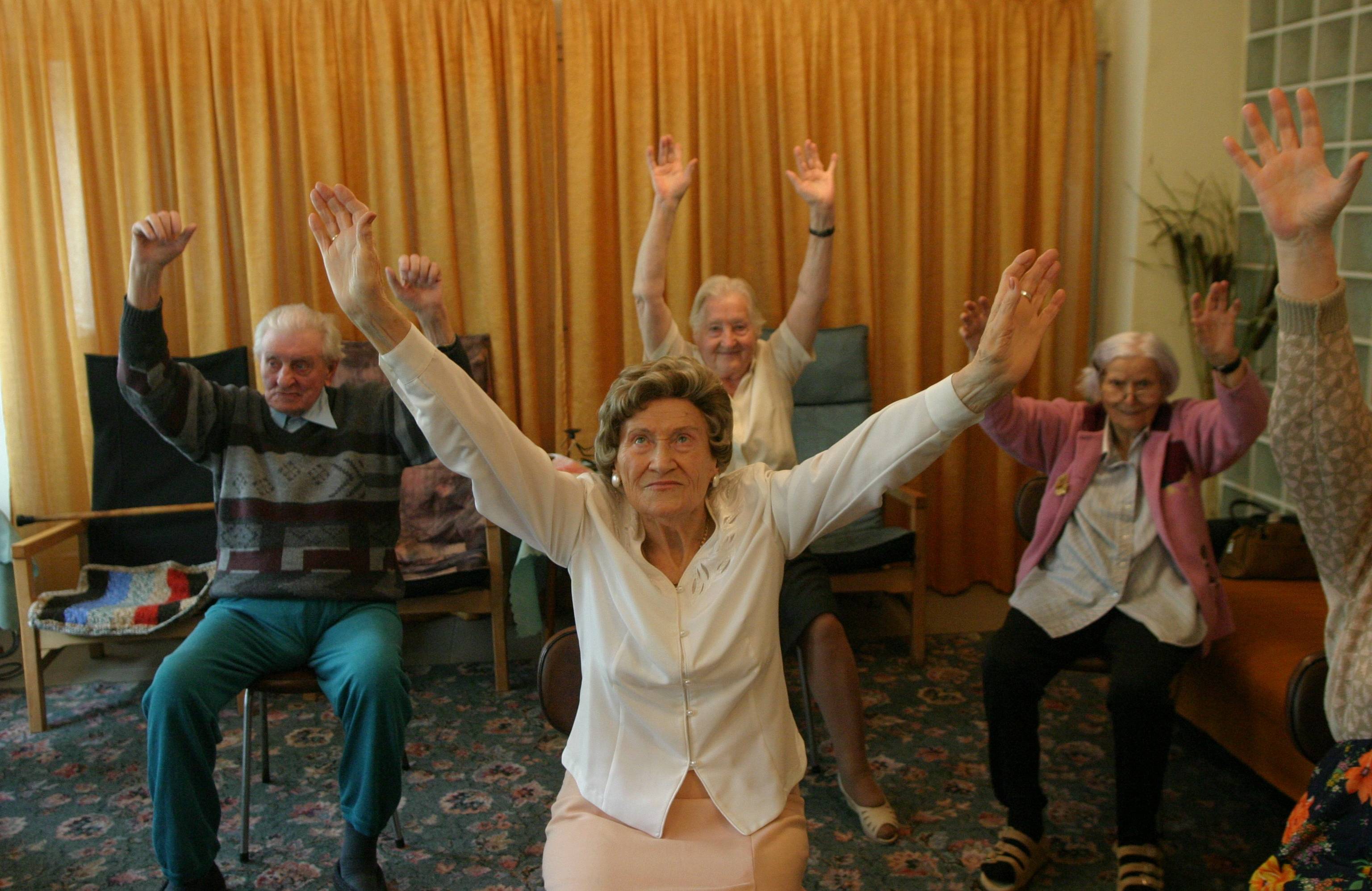 Kilka starszych osób podnosi ramiona w górę - w ramach aerobiku dla seniorów