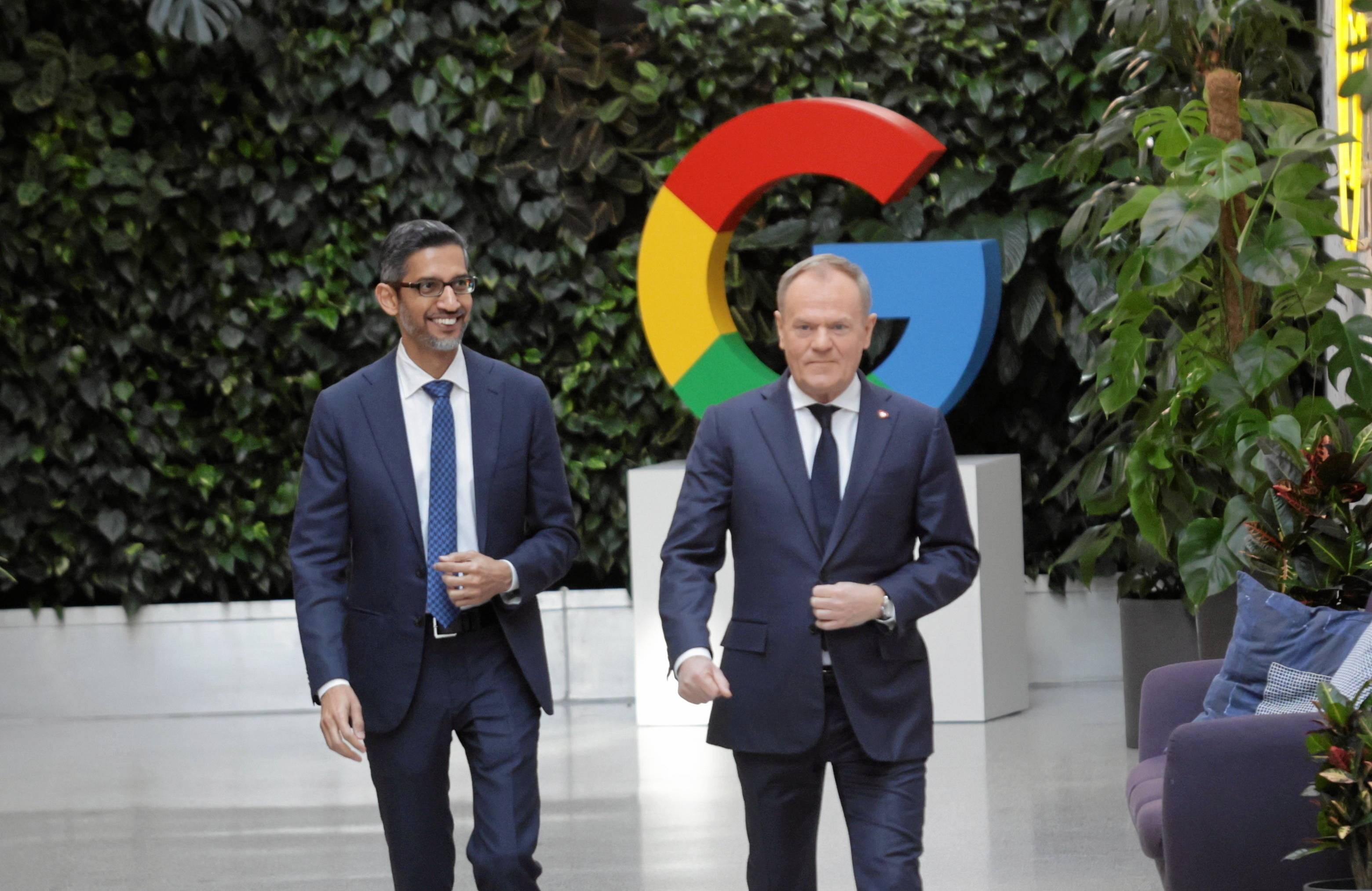Dwaj mężczyńi stoją na tle wielkiej litery G, znaku firmowego Googla