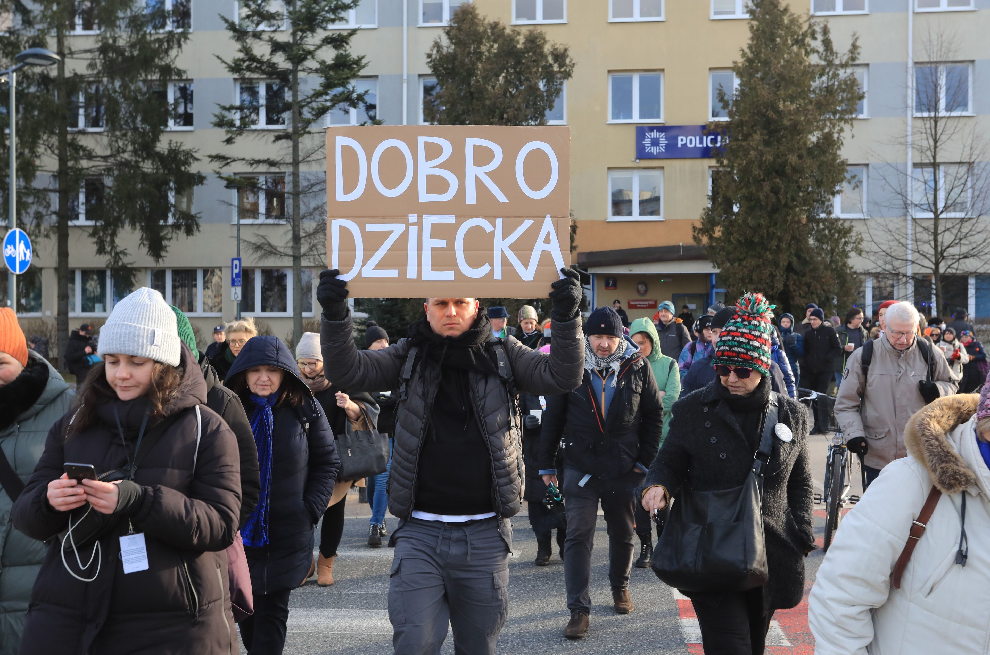 Demonstracja pod budynkiem policji. Jeden z demonstrantów trzyma karton z napisem "prawa dziecka"