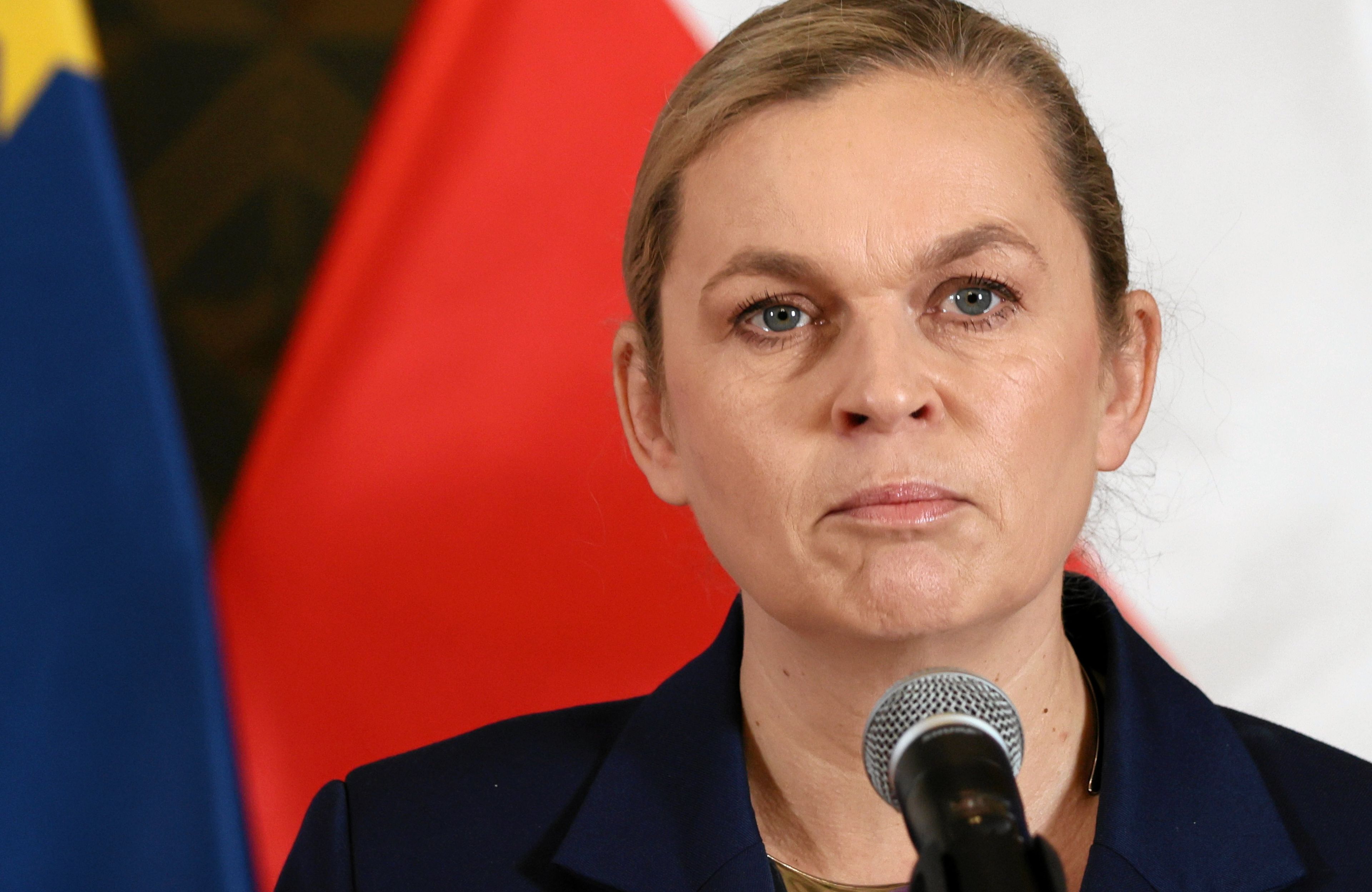 Kobieta (ministra Barbara Nowacka) stoi przed mikrofonem na tle polskiej i europejskiej flagi