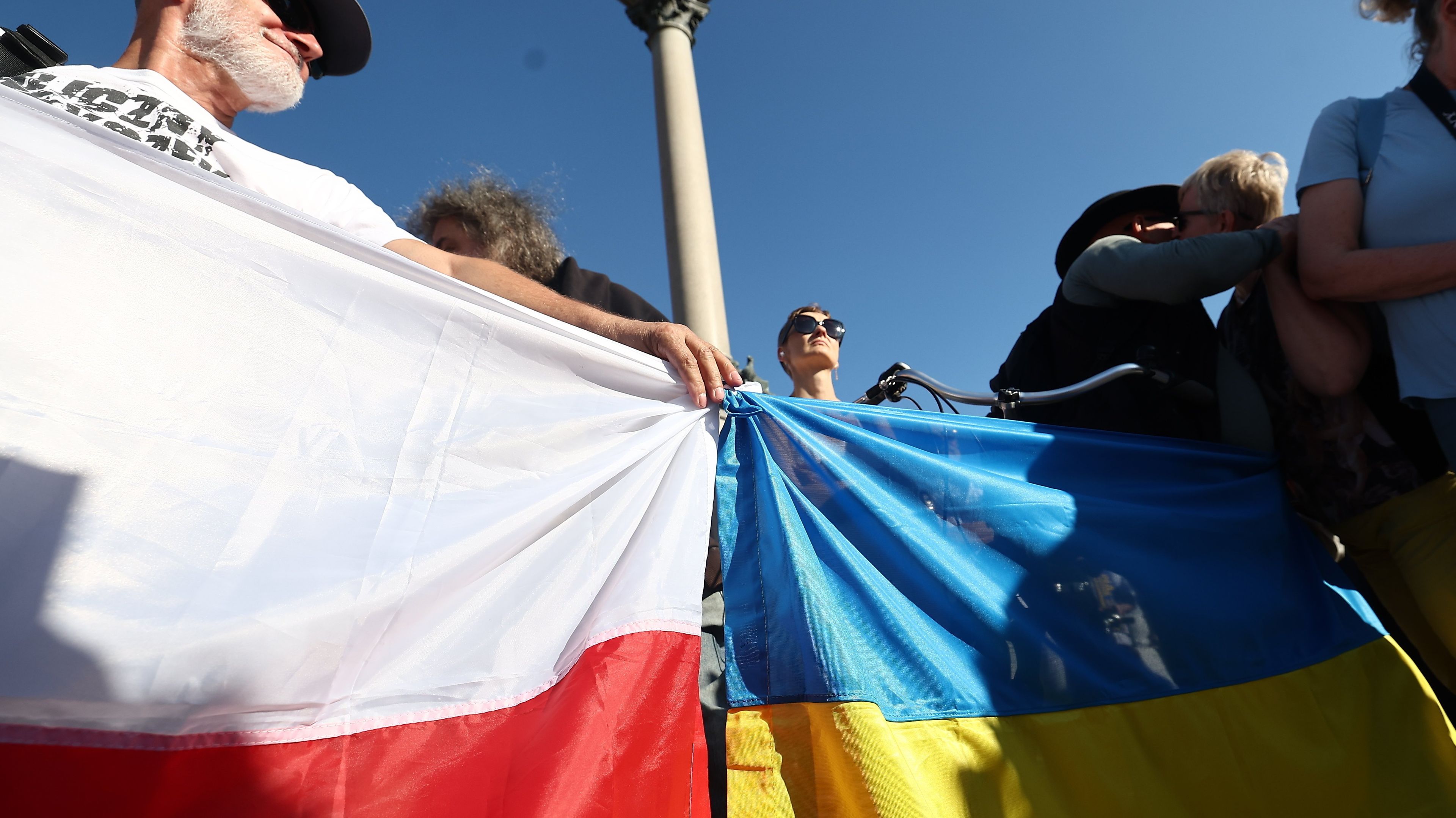 na zdjęciu widać osoby z manifestacji proukriańskiej pod kolumną zYGMUNTĄ na placu zamkowym, dwie osoby na pierwszym planie trzymają wielkie flagi - polską i ukraińską