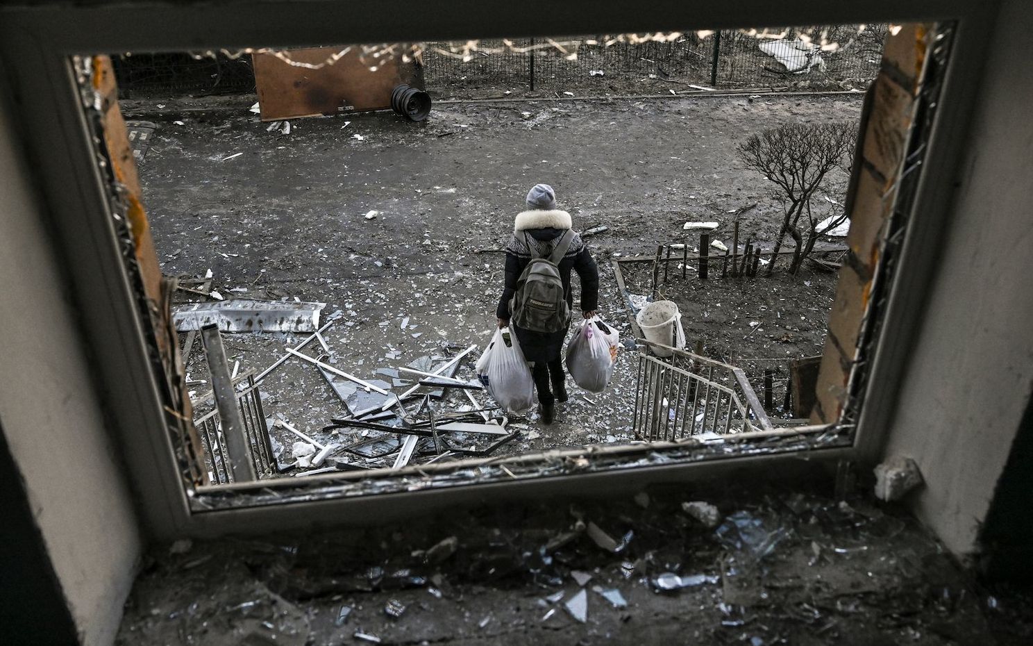 A woman collects her belongings from her destroyed apartment after shelling in Kyiv on March 18, 2022, as Russian troops try to encircle the Ukrainian capital as part of their slow-moving offensive. - Authorities in Kyiv said one person was killed early today when a downed Russian rocket struck a residential building in the capital's northern suburbs. They said a school and playground were also hit. (Photo by Aris Messinis / AFP)
