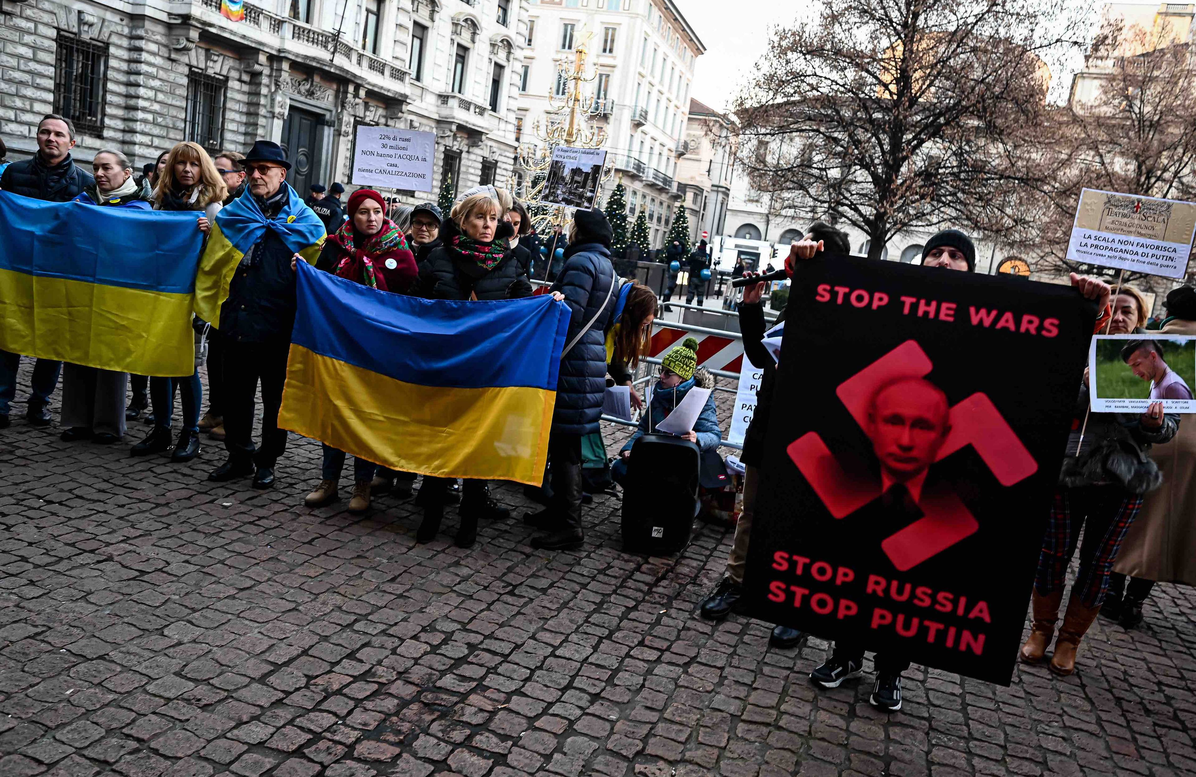 Protestujący na ulicy trzymają ukraińskie flagi oraz plakat z twarzą Putina wpisaną w czerwoną swastykę na czarnym tle i napisem Stop War - Stop wojnie. Rosjanie
