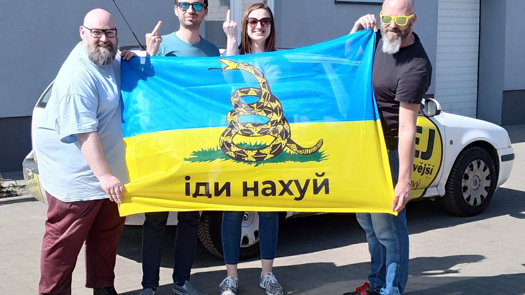 Kilka osób trzyma flagę Ukrainy z napisem Idi na chuj
