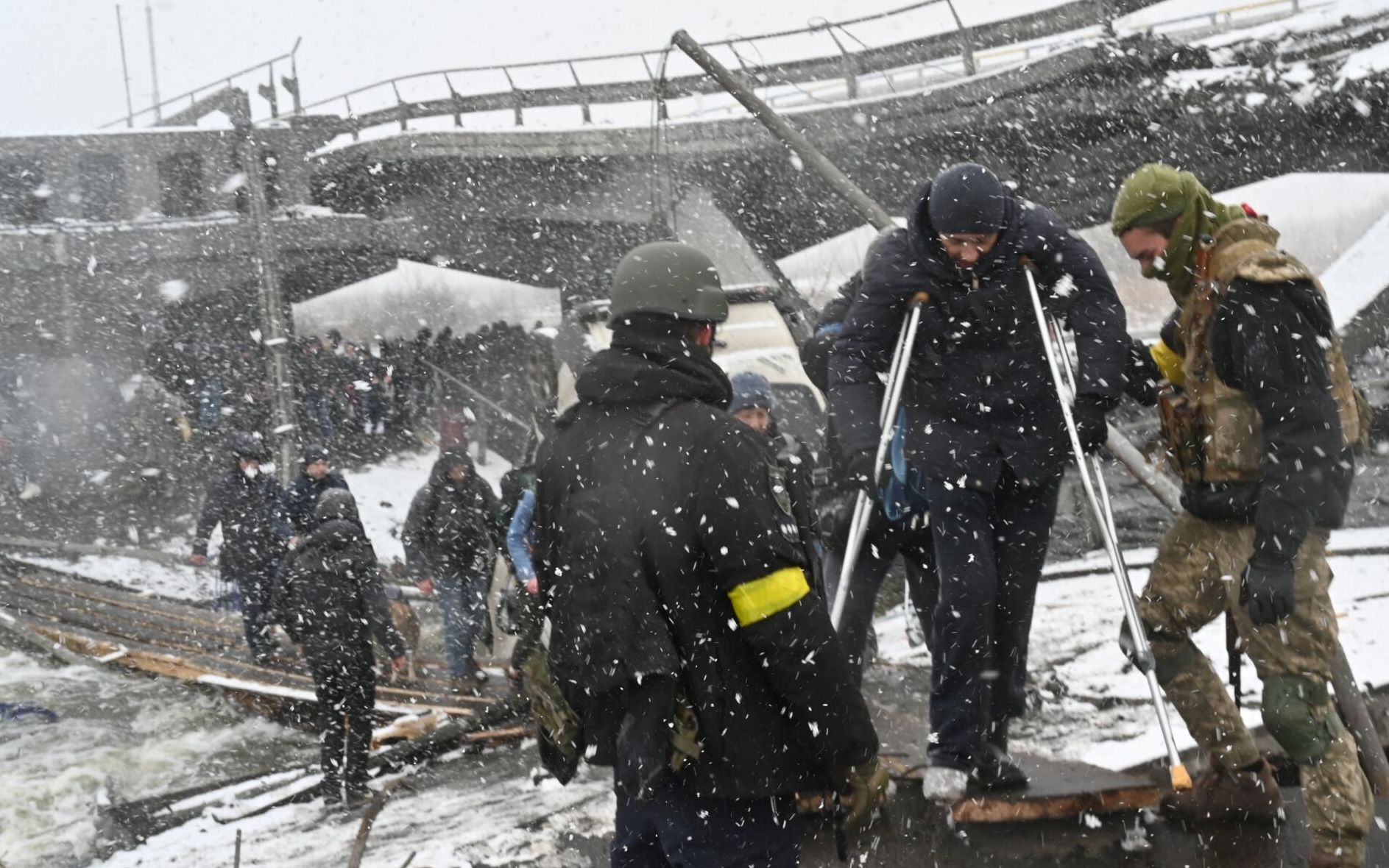 Ukrainian soldiers help a disabled man to cross a destroyed bridge during the evacuation by civilians of the city of Irpin, northwest of Kyiv, on March 8, 2022. - More than two million people have fled Ukraine since Russia launched its full-scale invasion less than two weeks ago, the United Nations said on March 8, 2022. (Photo by Sergei SUPINSKY / AFP)
