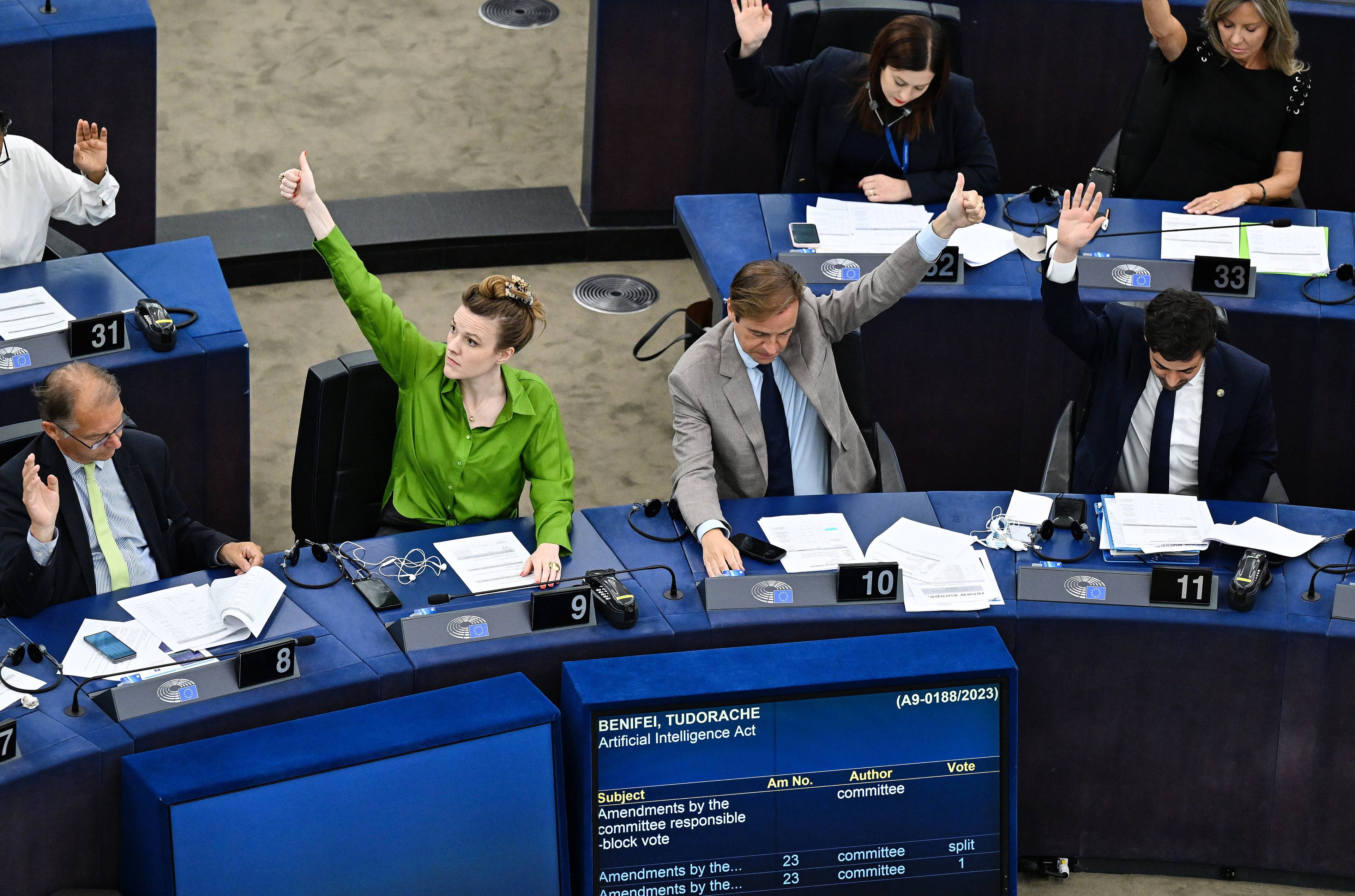 Sala Parlamentu Europejskiego. Kobieta w zielonej bluzce głosuje prawą ręką, a mężczyzna w szarym garniturze - podnosi rękę lewą