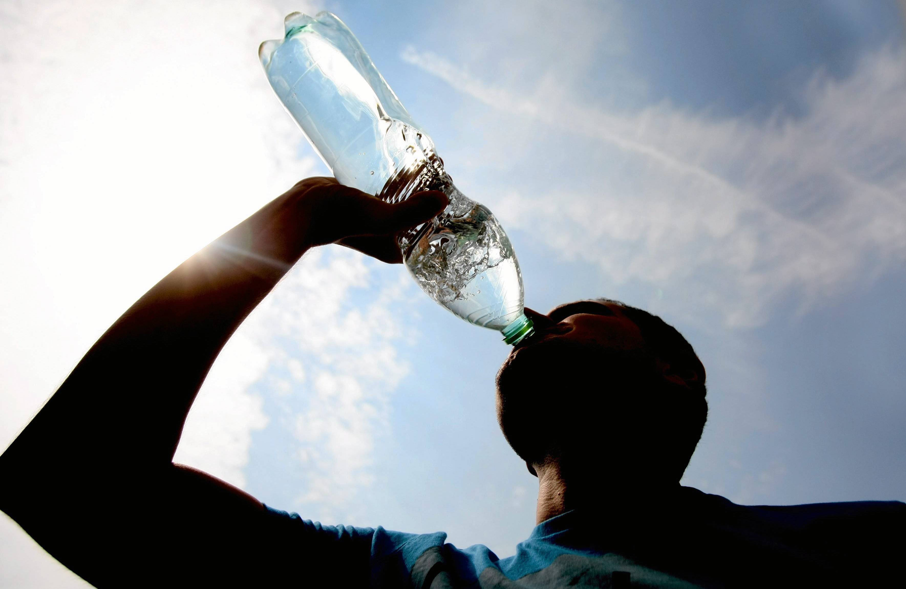 Mężczyzna pije wodę z butelki na tle rozżarzonego gorącego dnia
