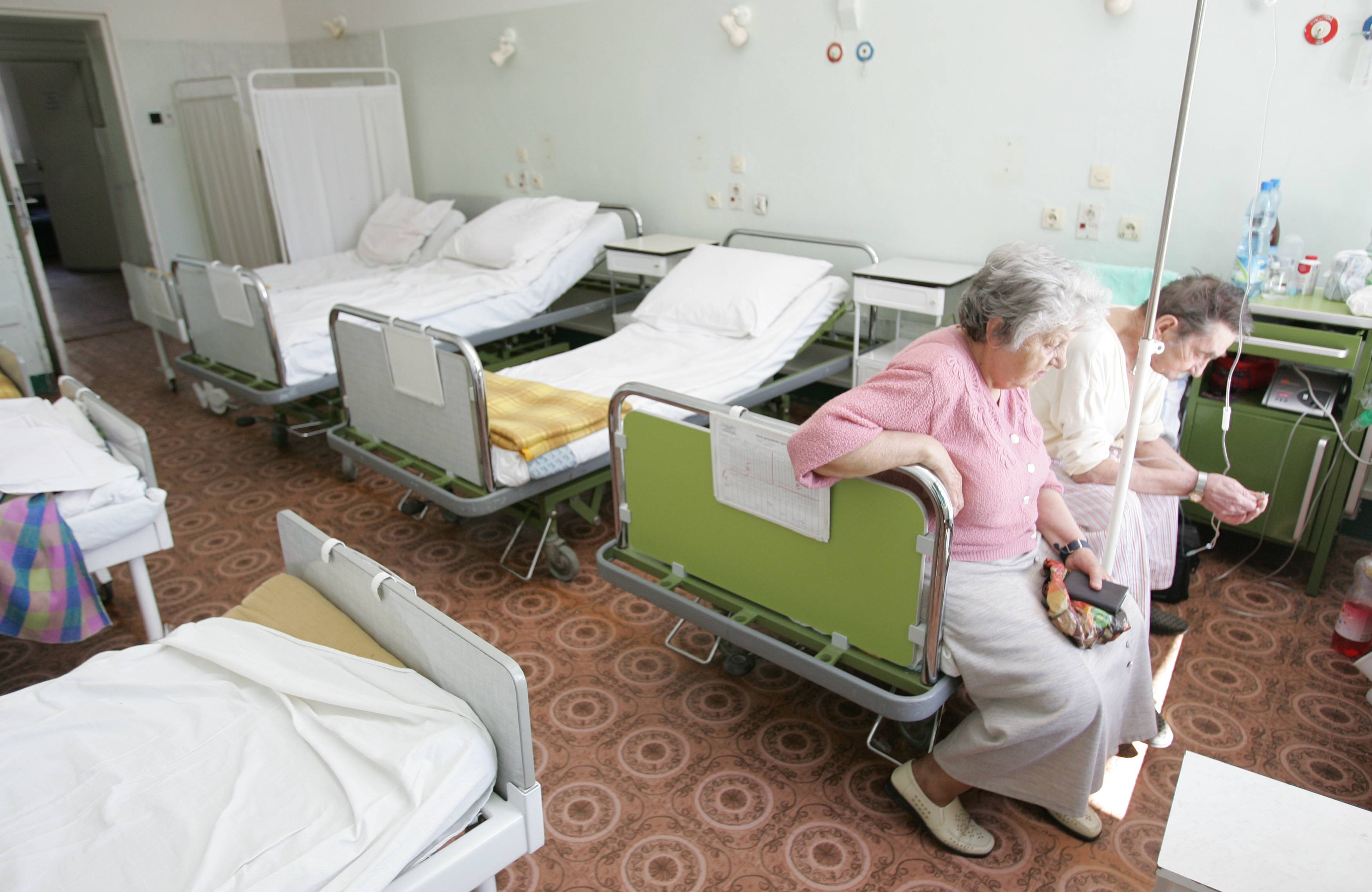 Pusta sala szpitalna. Dwie starsze kobiety siedzą na jednym łóżku