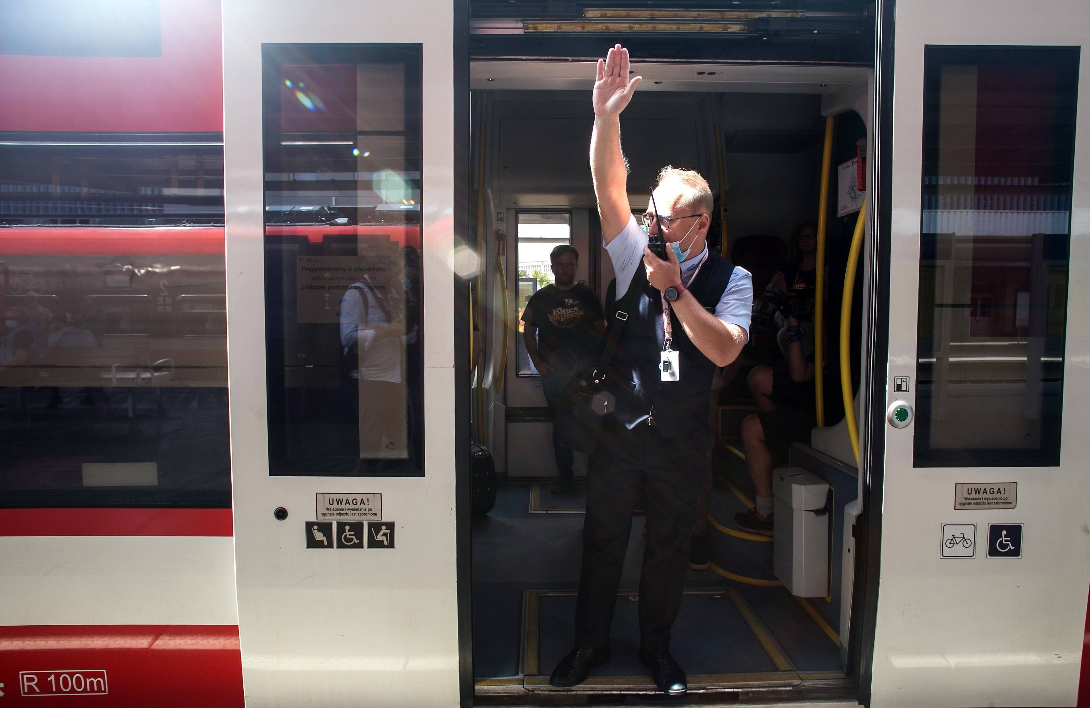 konduktor z krótkofalówką i wyciągniętą ręką ogłasza odjazd w drzwiach pociągu