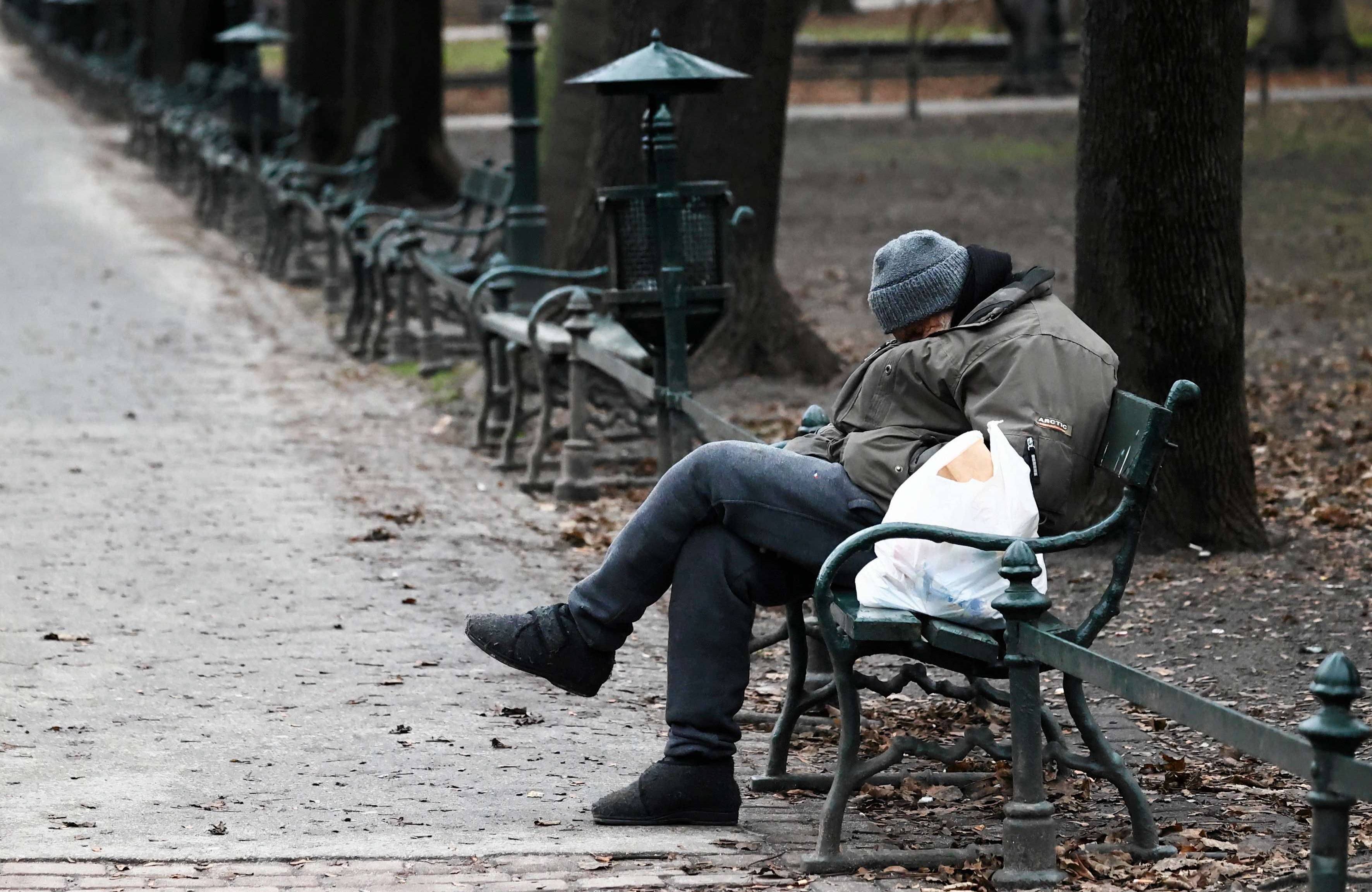 Bezdomny śpi na siedząco na ławce na krakowskich Plantach