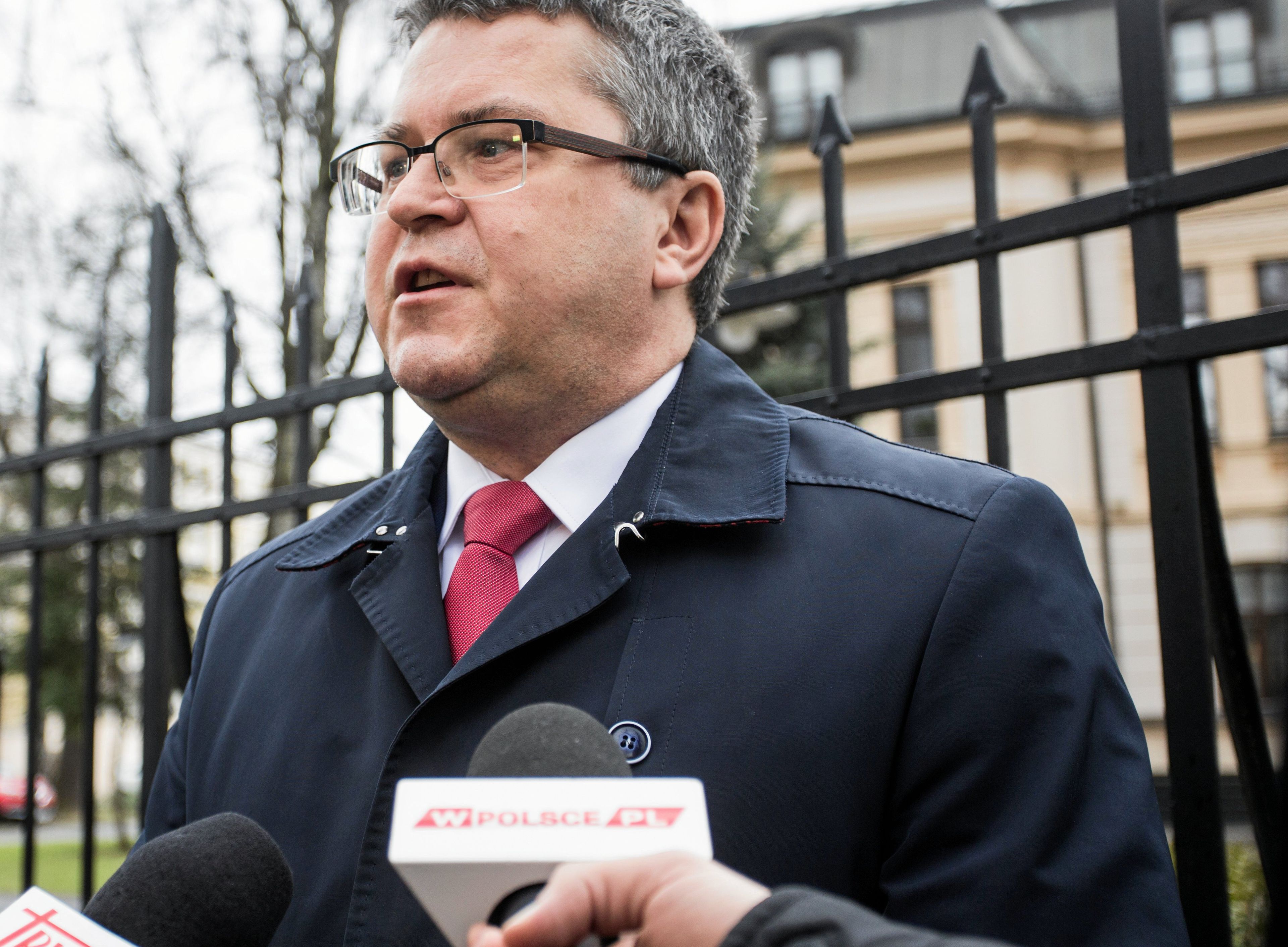 Mężczyzna w okularach stoi na tle metalowego płotu Trybunału Konstytucyjnego. Jarosław Dudzicz