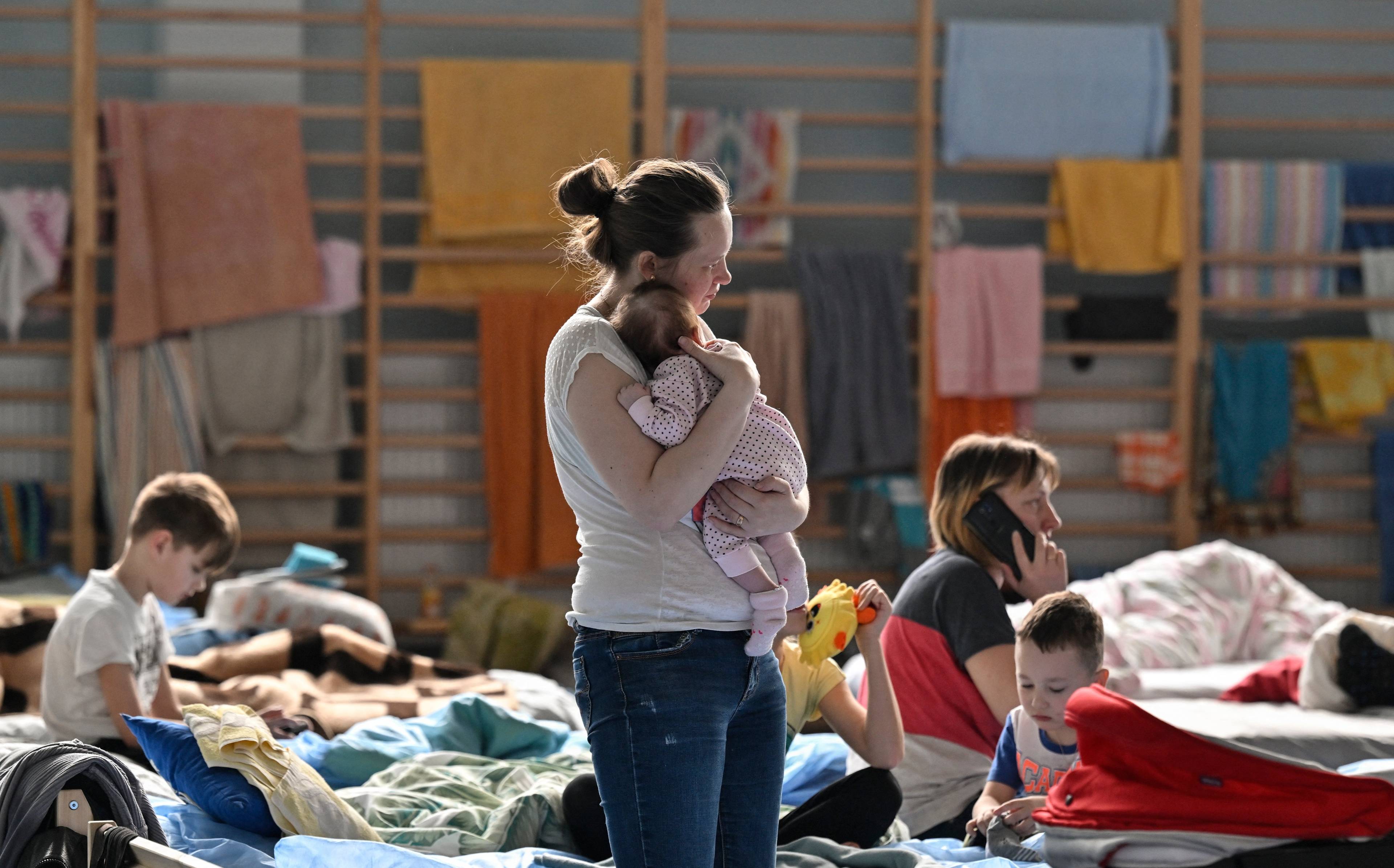 Kobieta trzyma na rękach niemowlaka, w tle łóżka, na których siedzą inne kobiety