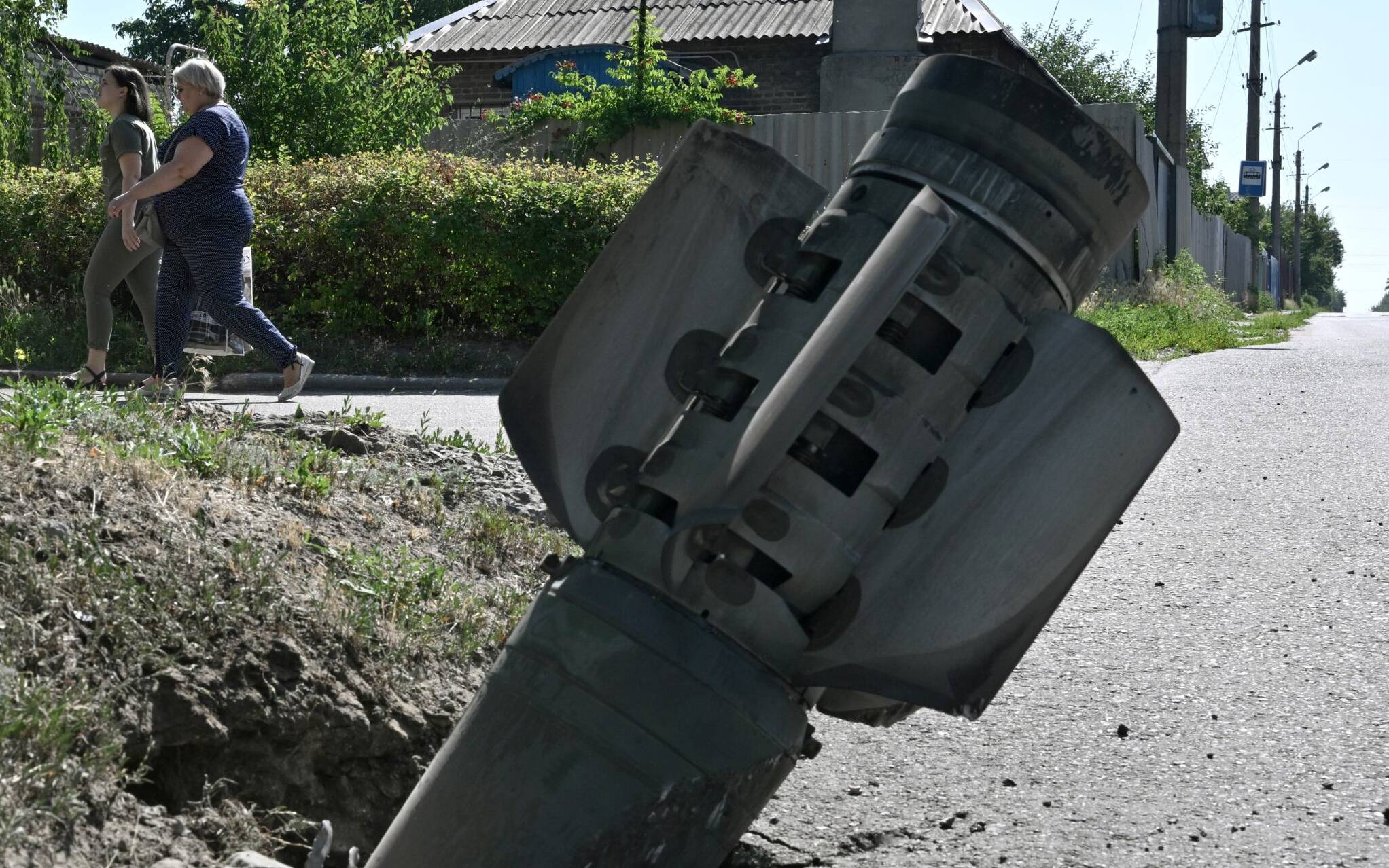 Pedestrians walk past the tail section of a rocket which is embedded in the ground, in Kramatorsk on July 4, 2022, the day after a Russian rocket attack. (Photo by Genya SAVILOV / AFP)