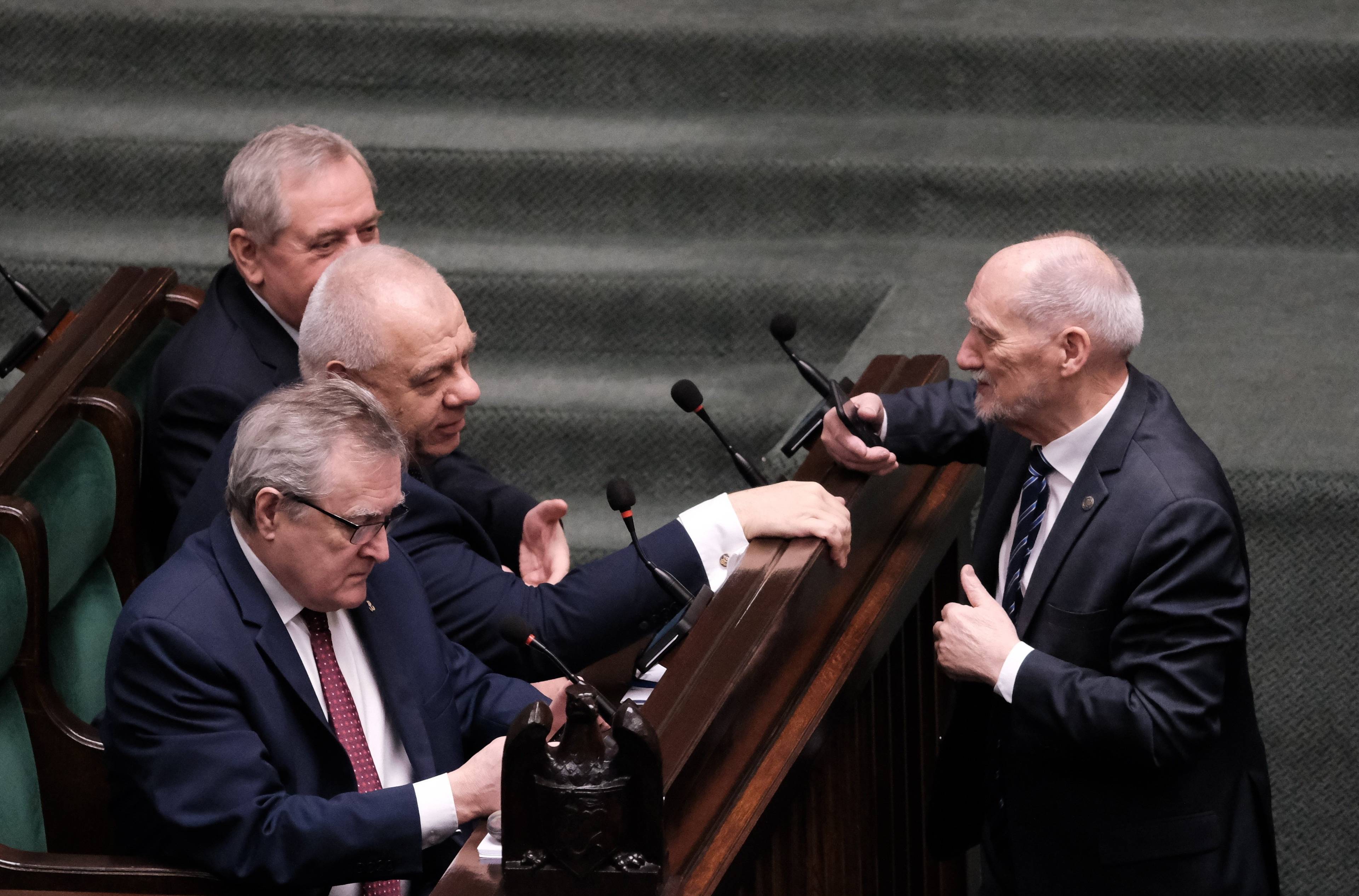 Antoni Macierewicz stoi przed ławami rządowymi w Sejmie i rozmawia z Jackiem Sasinem