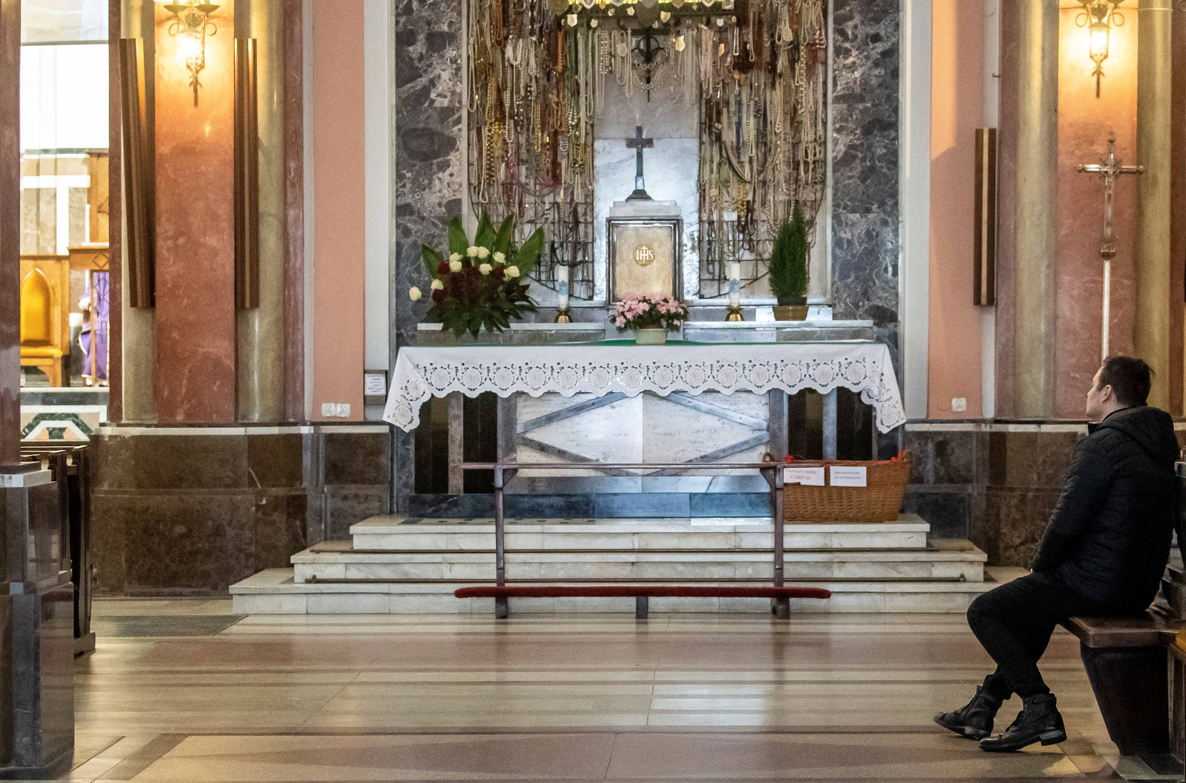Pusta przestrzeń przed ołtarzem w kościele, z boku na ławce siedzi jeden mężczyzna