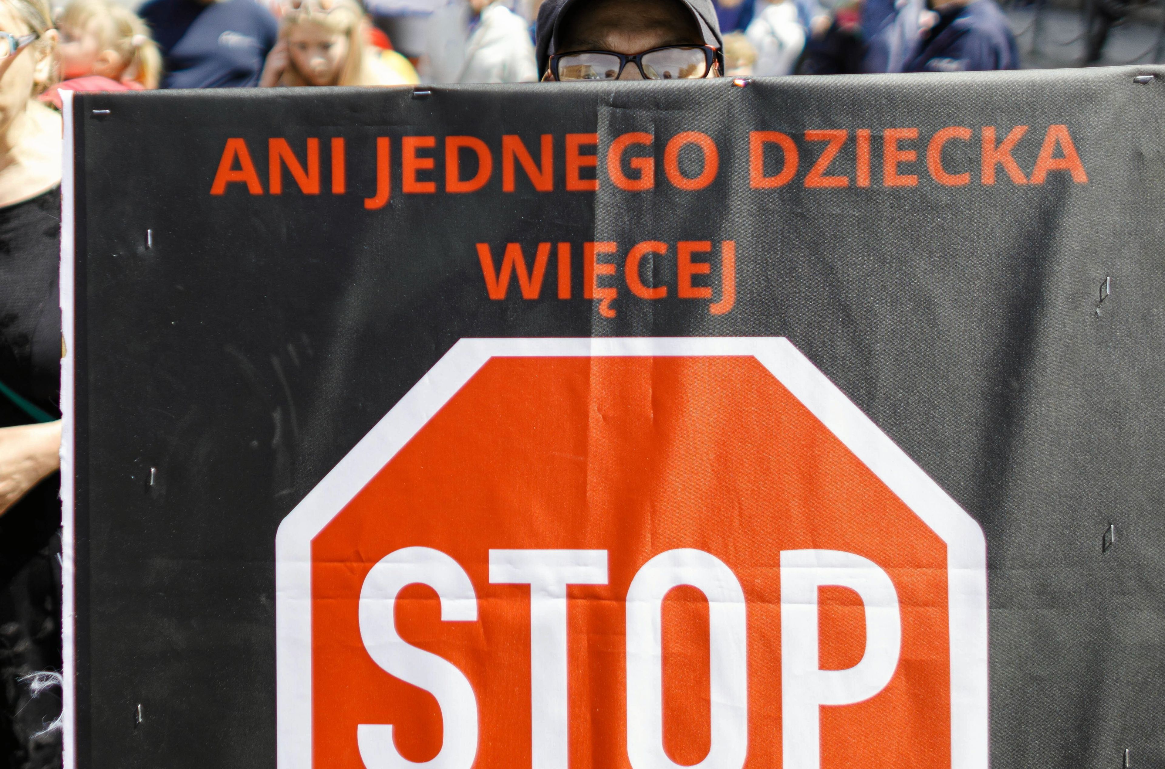 Mężczyzna trzyma plakat przeciw przemocy w rodzinie. Napis: "Ani jednego dziecka więcej. STOP"