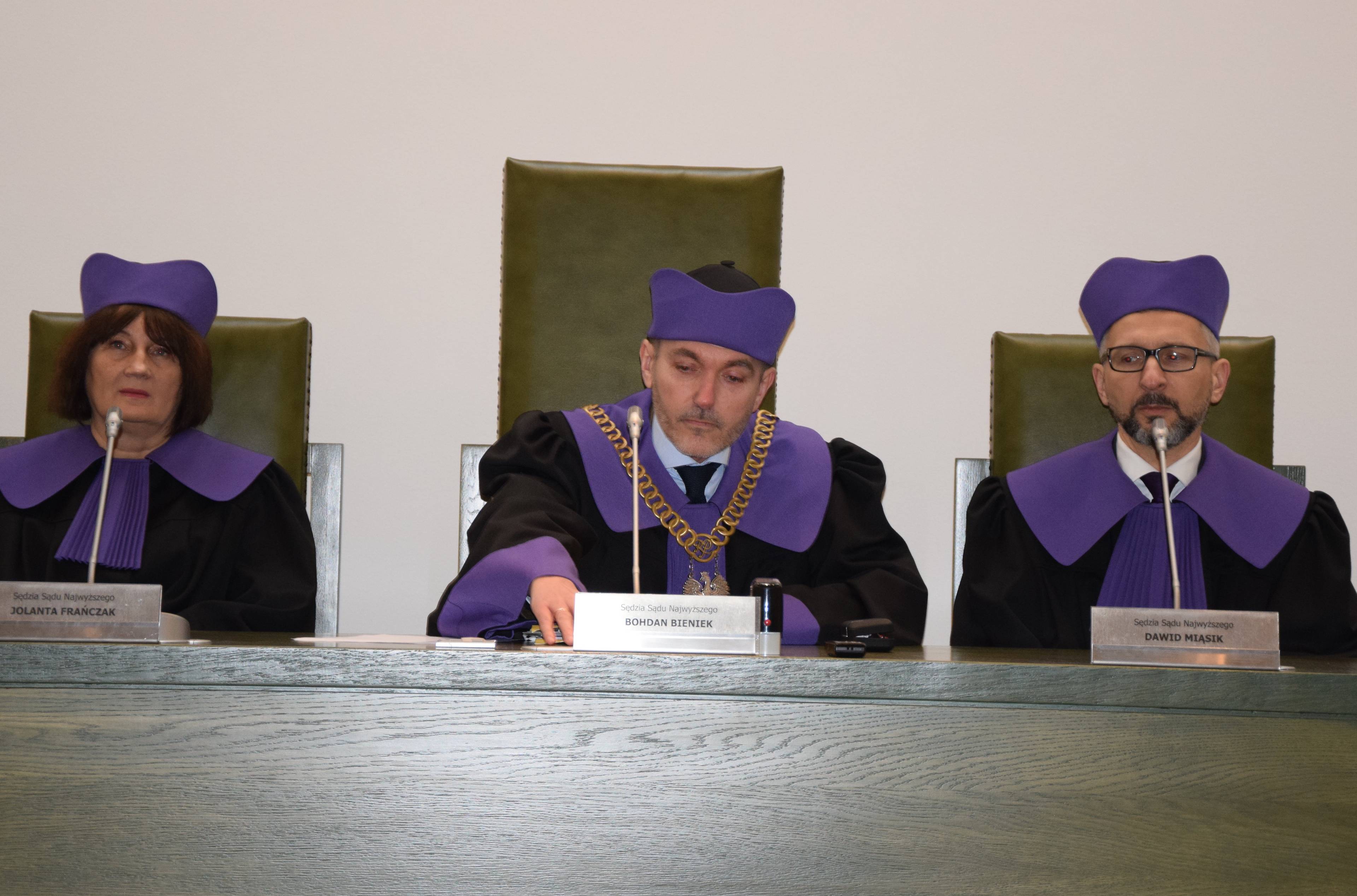 Trzy osoby w sędziowskich togach za stołem sędziowskim
