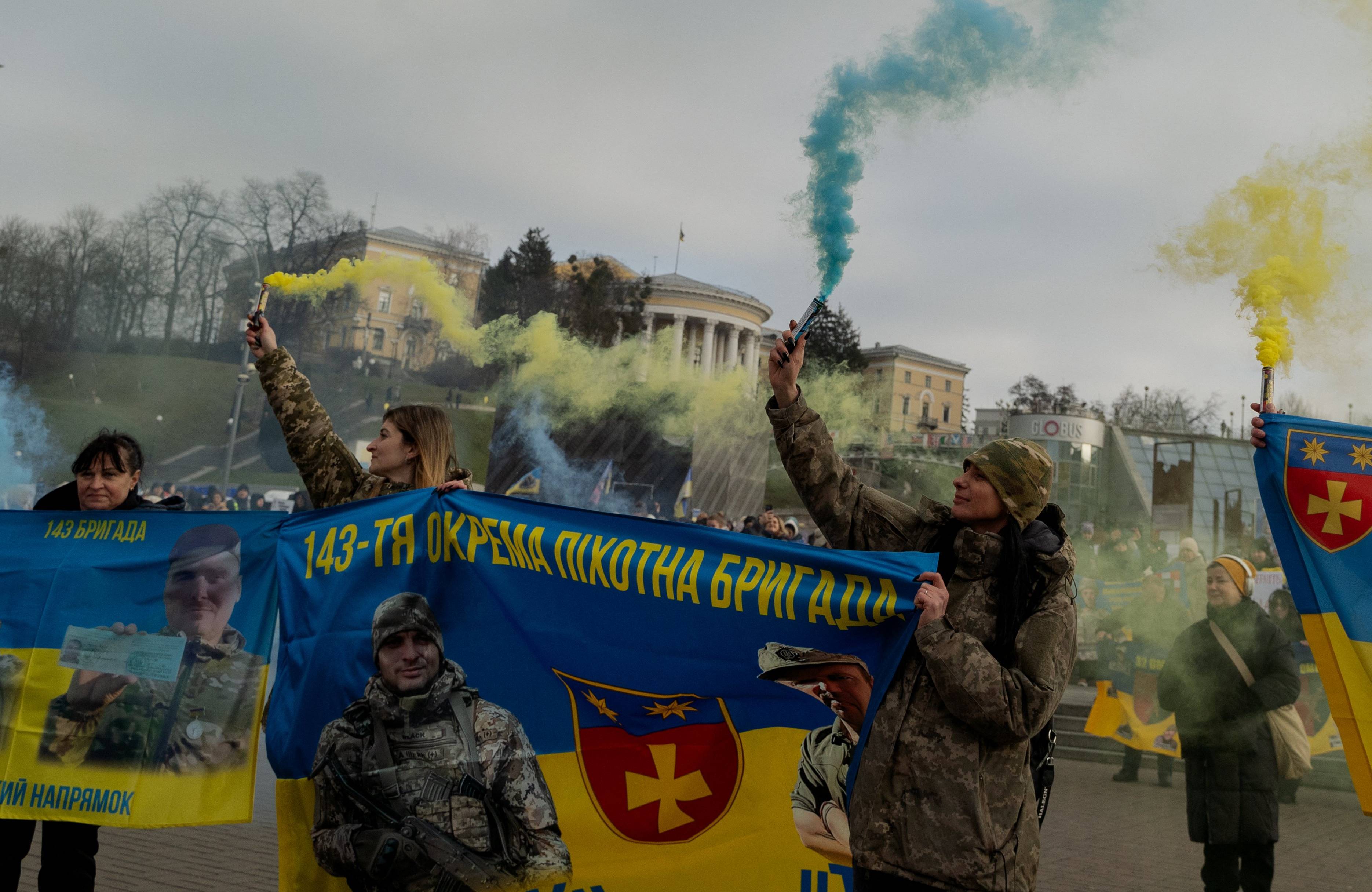 Protestujący ze sztandarem ukraińskiej brygady piechoty i niebieskimi oraz żółtymi flarami.