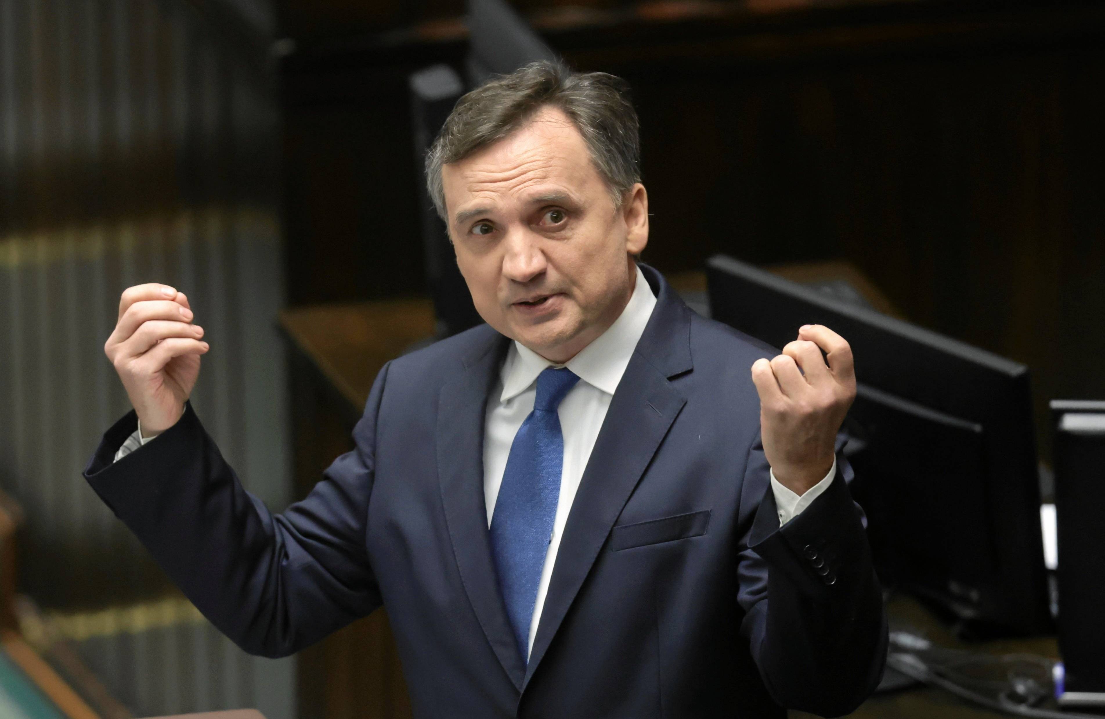 Minister Zbigniew Ziobro podnosi w górę ręce na mównicy sejmowej