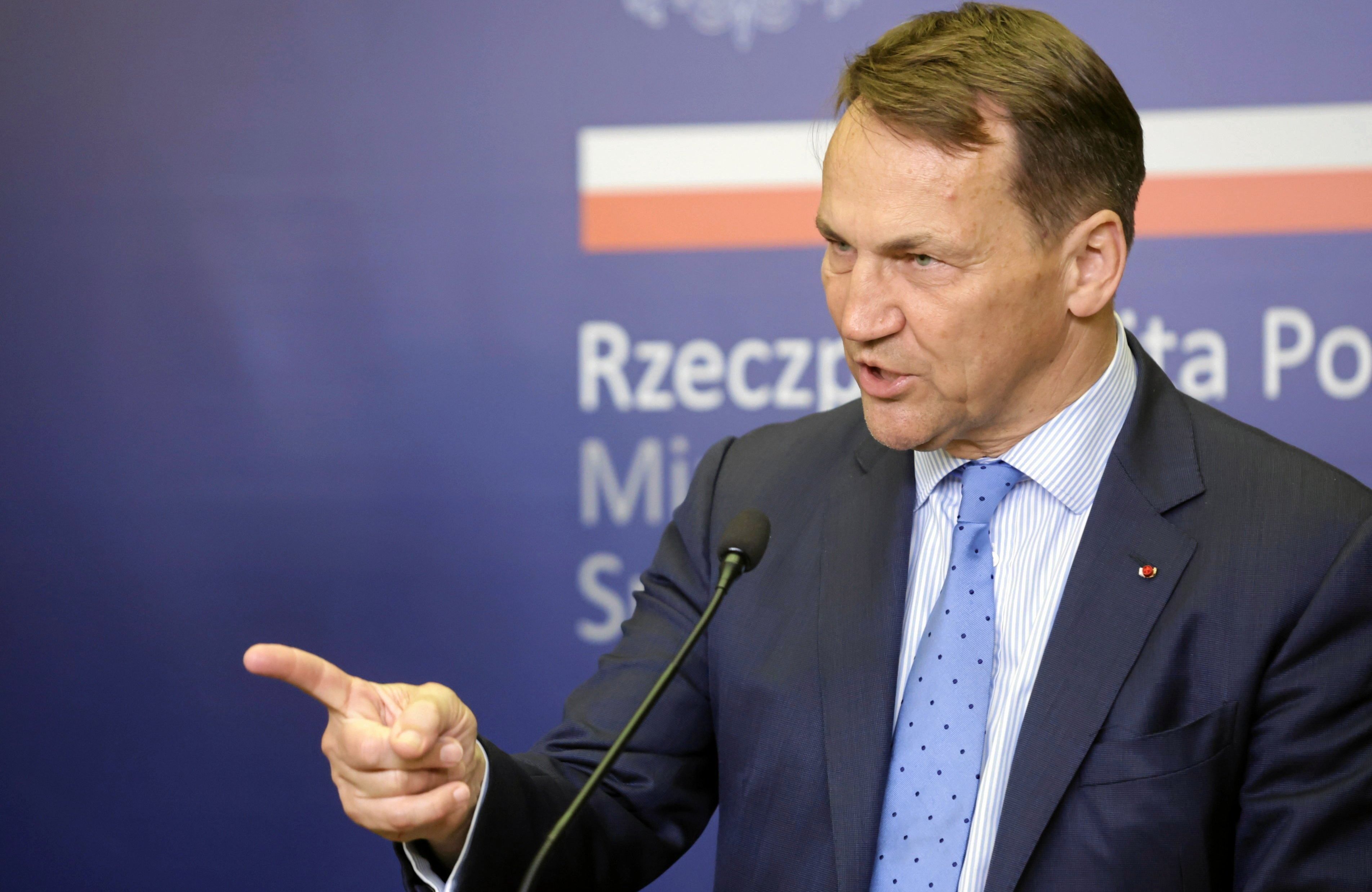 Na zdjęciu jest mężczyzna ok. 60-lat. Jest ubrany w garnitur, ma też jasną koszulkę i błękitny krawat. Przemawia do mikrofonu