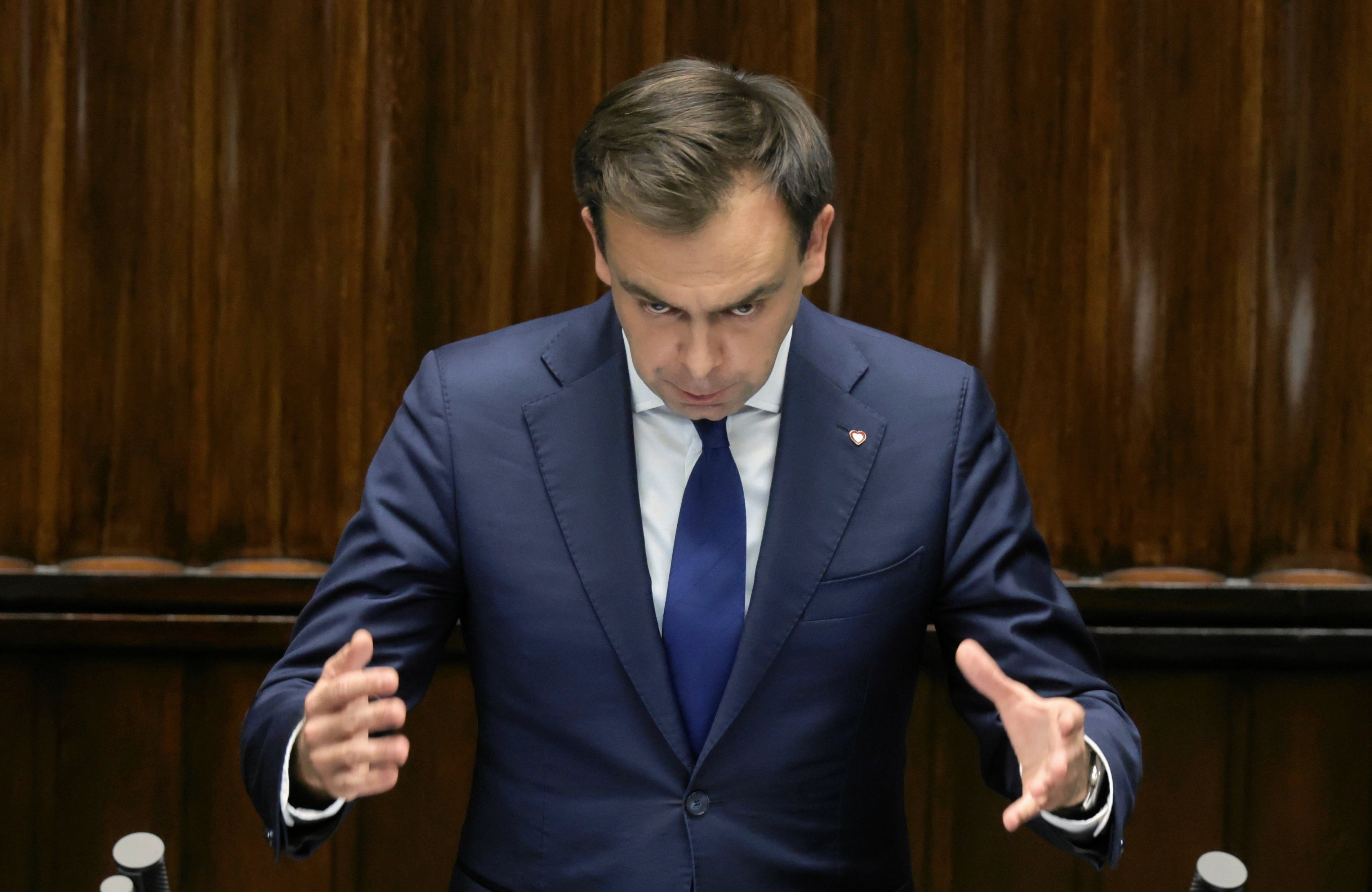 Mężczyzna w garniturze pochylony z rozchylonymi rękami, jakby był czarodziejem