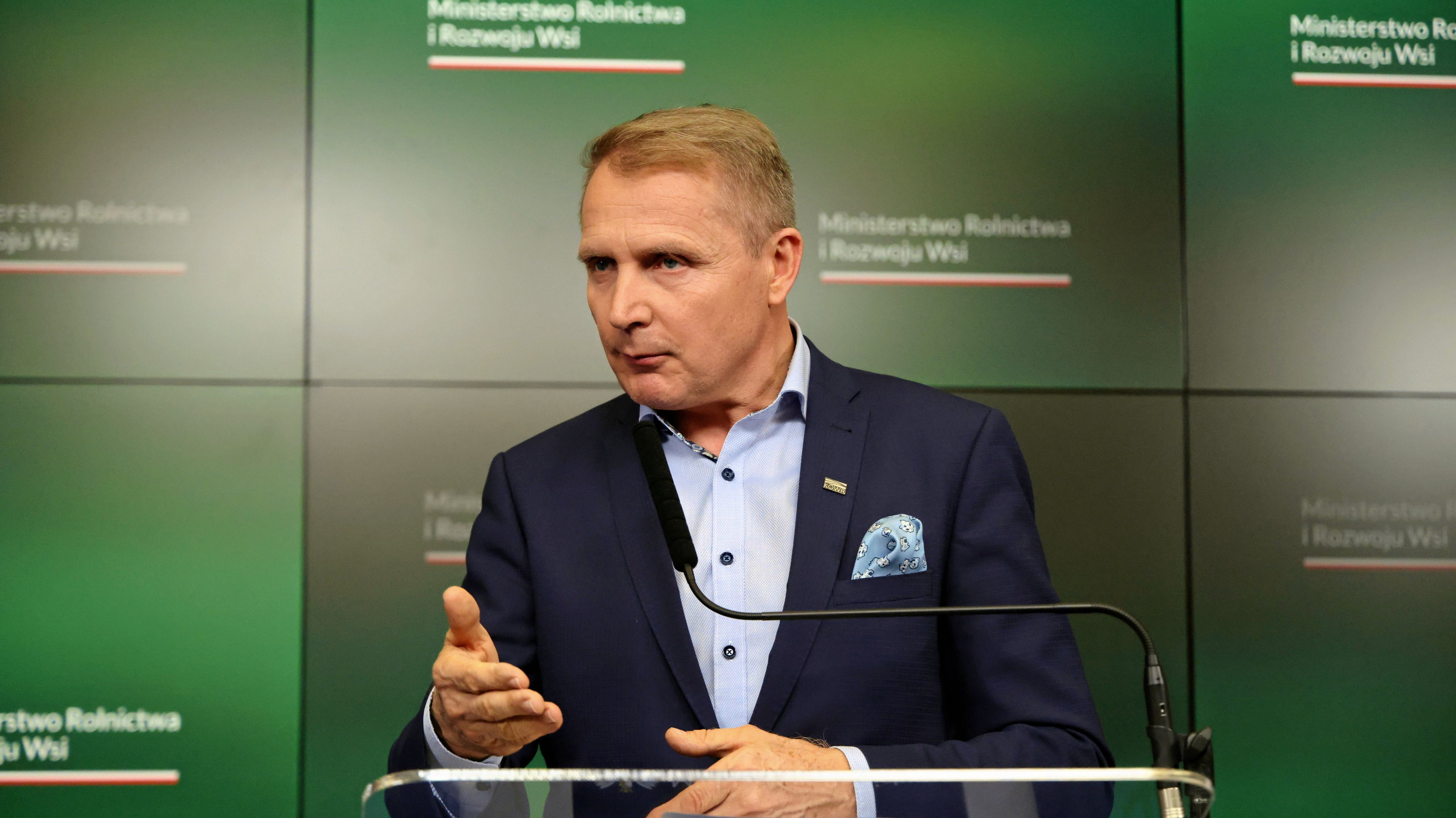 szef KOWR Henryk Smolarz w marynarce na tle zielonej planszy w czasie konferencji prasowej