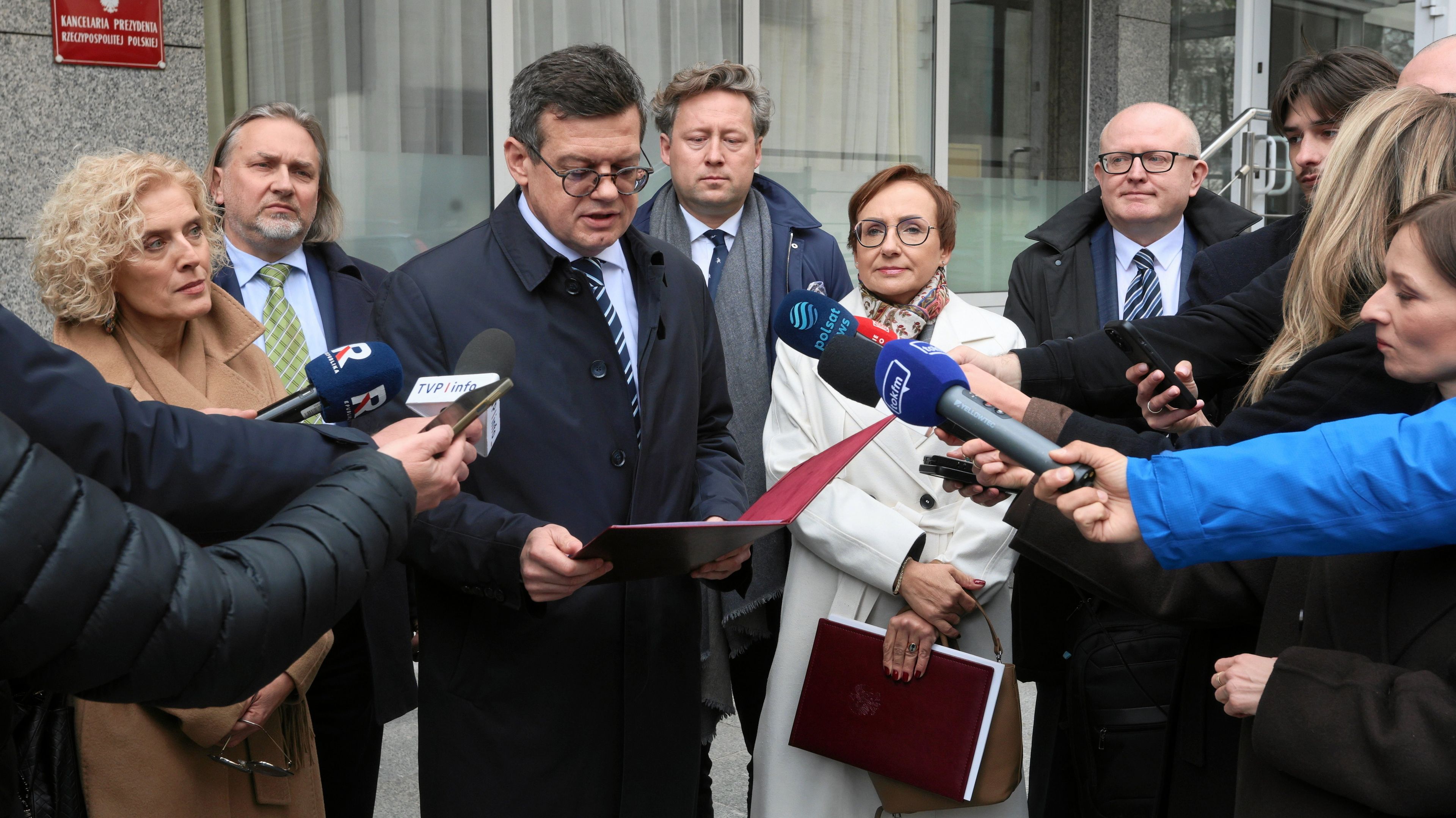 Kilka osób stoją w szeregu przed dziennikarzami